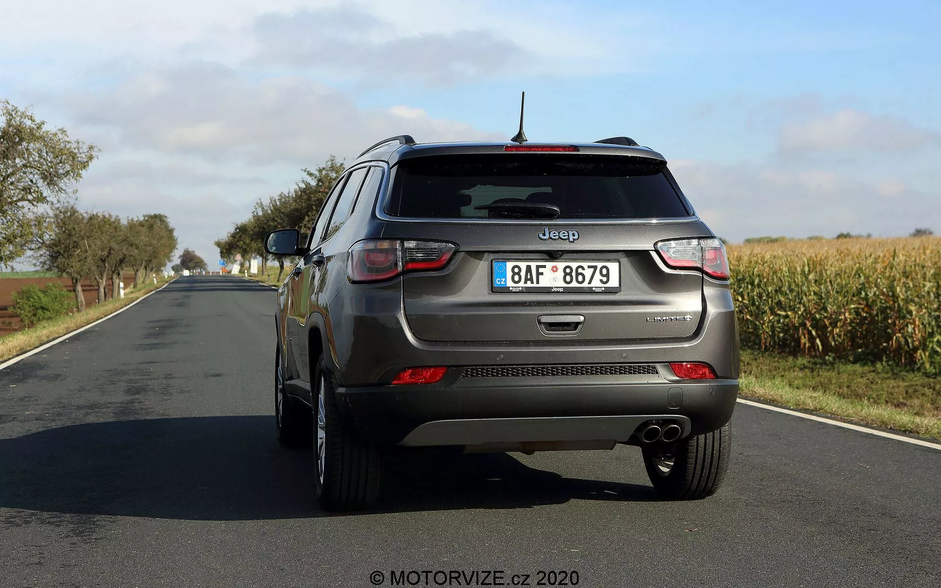 Bakre trekvartsvy av en Jeep Compass 2017 som visar distinkta designelement inklusive bakljus, bakre stötfångare, dubbelt avgasrör, märkning på bakluckan, bakrute torkare, reflekterande remsa, fem-ekrade lättmetallfälgar, takmonterad antenn och reflexer på den nedre kanten. Bilden ger en tydlig vy bakifrån och något från förarsidan med gott om utrymme mellan bilen och kameran.