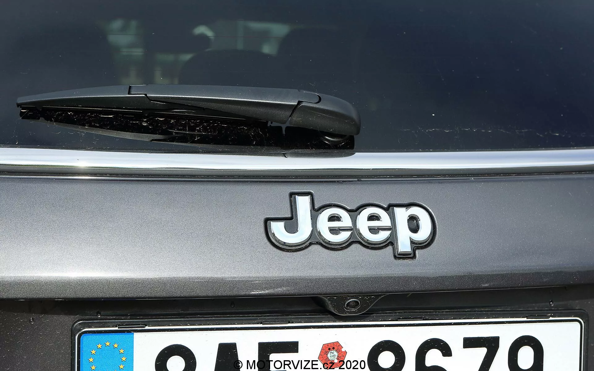 Närbild av bakre delen av en Jeep Compass 2017 med centrerad Jeep-logotyp, bakre vindrutetorkare och delvis synlig europeisk registreringsskylt med suddig landsidentifierare