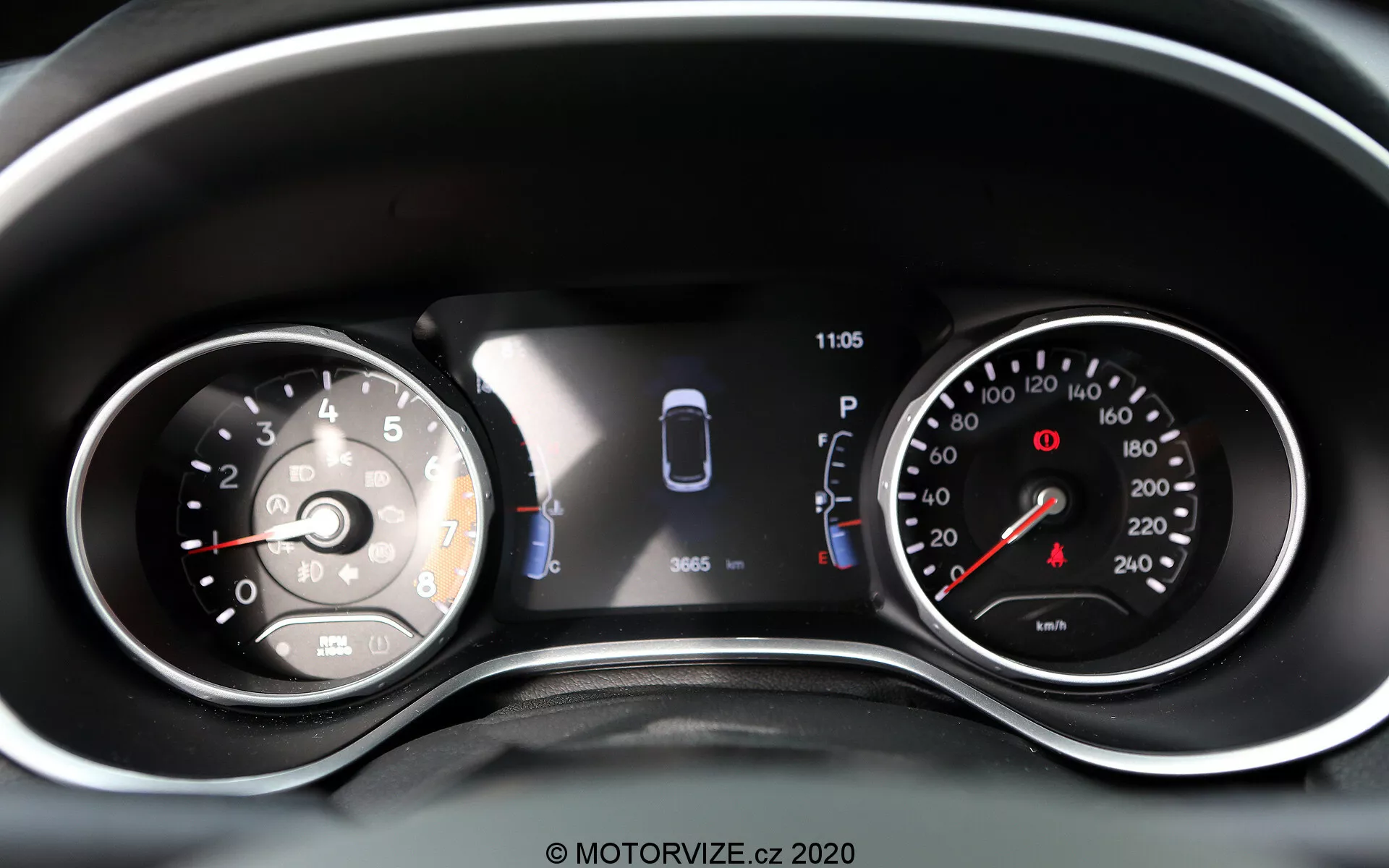 Närbild av instrumentpanelen i Jeep Compass 2017 som visar en kombination av analoga mätare och en digital display. Till vänster finns en analog hastighetsmätare markerad upp till 260 med en nål som pekar precis ovanför 0. Den centrala digitala displayen visar en grafisk representation av bilen med sensorer och två öppna dörrar, vilket indikerar parkeringsassistans och fordonsstatus. En klocka visar 11:05. Till höger finns en analog varvräknare med röd zon som börjar före 7, markerad upp till 8 (1 000 varv/minut). Ytterligare varningslampor och ikoner är synliga, vilket gör detta till en väl upplyst och tydlig representation av fordonets moderna och traditionella avläsningar samt förarassistanssystem.