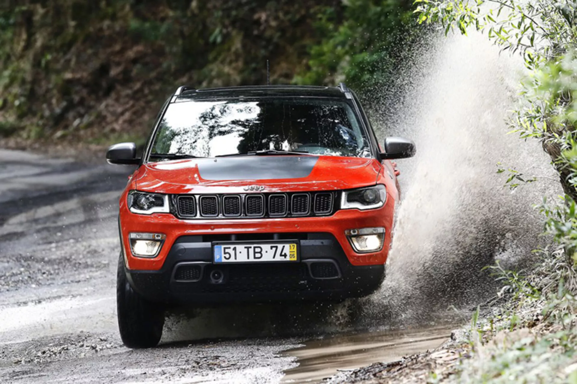 Röd Jeep Compass SUV från 2017 kör på en blöt grusväg, visar framgaller, LED-strålkastare och off-road förmåga med vattenstänk