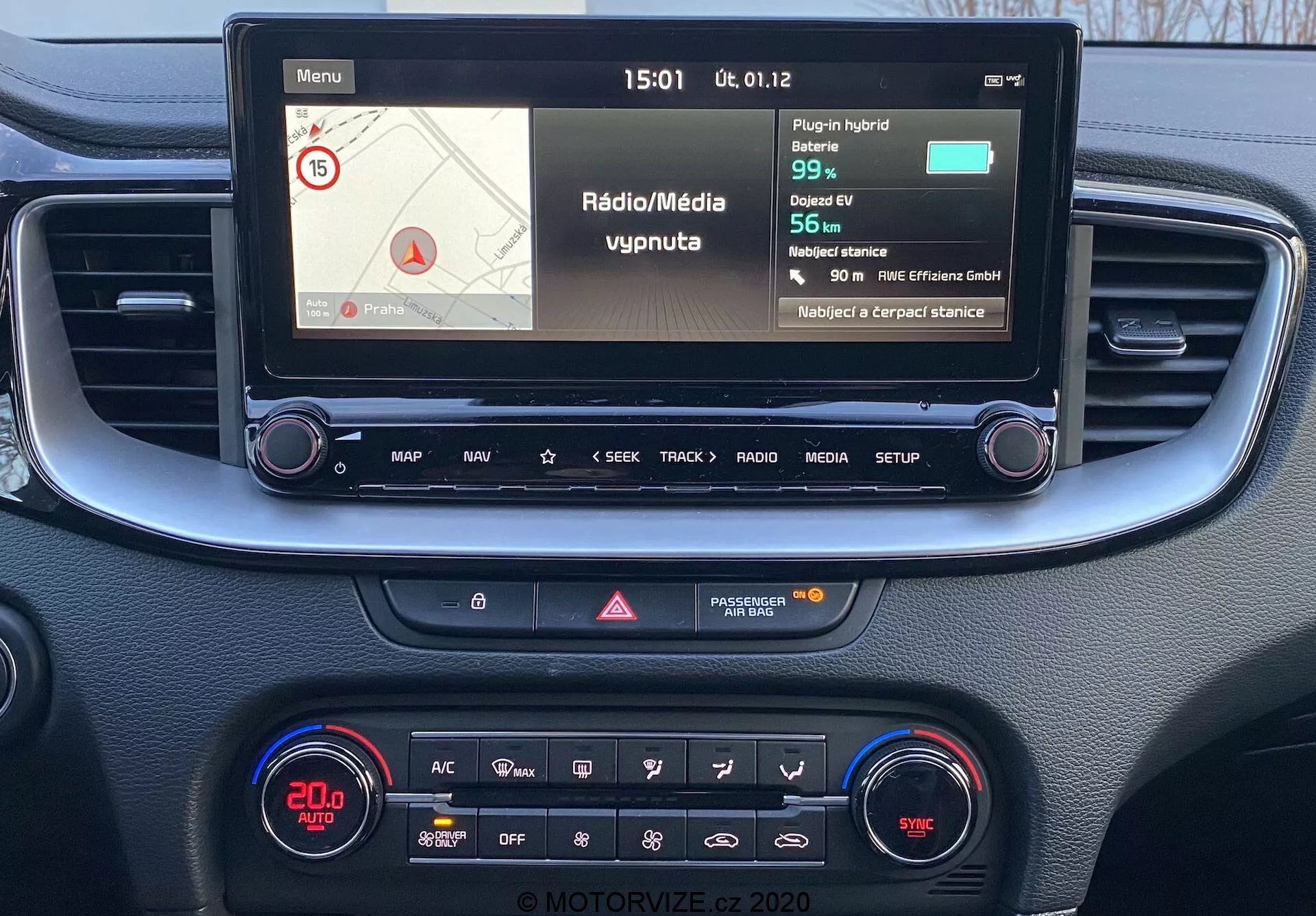Förarperspektiv av mittkonsol och infotainmentsystem i Kia Ceed 2018, med en färgskärm som visar navigations- och medieinformation, fysiska knappar för kontroll och en klimatkontrollpanel med digital display och olika funktioner.