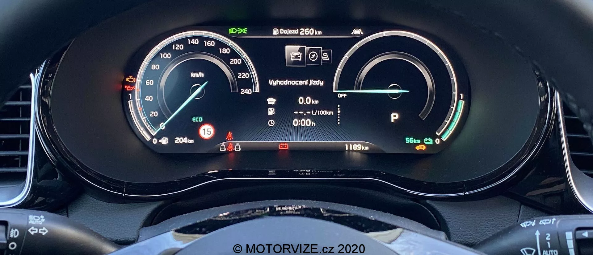 Närbild av Kia Ceed 2018 digitala instrumentbräda från förarens säte. Displayen inkluderar en hastighetsmätare med en fysisk nål och digital avläsning, visande 15 km/h. Till höger finns en energibatterimätare som visar en fulladdad batteri med en räckvidd på 481 km. Andra element inkluderar en redo-statusvisning, förarinformation med varningslampor, en utetemperatursläning på 20,5°C och fordonet i park. Ratten är synlig med en sportig, platt botten design.