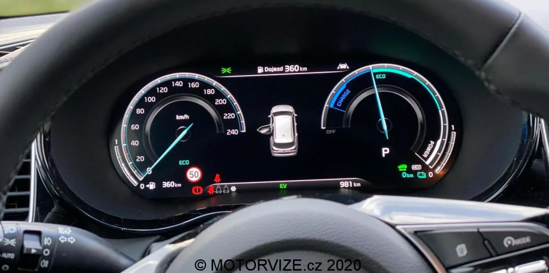 Närbild av Kia Ceed 2018:s digitala instrumentbräda från förarens synvinkel, med en stor widescreen-skärm och detaljerade instrument inklusive en hastighetsmätare upp till 260 km/h, effektmätare med Eco, Comfort och Power-lägen, däcktrycksvarning och 'Park'-läge indikator. Instrumentbrädan visar också ett 360-graders kamerasystem och en odometer som visar 9811 km. Den omgivande kanten minskar bländning och rattens knappar är delvis synliga. Vattenstämpel 'MOTORVIZE.cz 2020'.