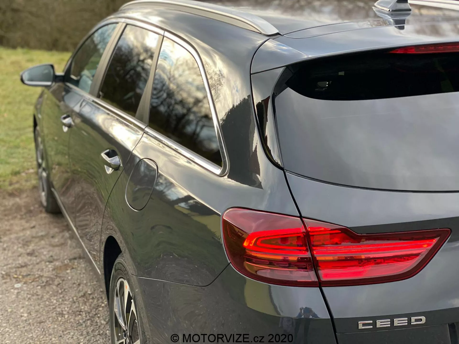 Delvis sida och bakvy av en modern, gråfärgad Kia Ceed 2018 hatchback-bil som betonar den upplysta C-formade LED-bakljuset, hatchback-design med bakrutetorkare och subtil takspoiler, hajfensantenn, lättmetallfälgar och varumärkesemblem med modellnamnet 'CEED', fångat i naturligt eftermiddagsljus och med ett grunt skärpedjup som fokuserar på fordonet.