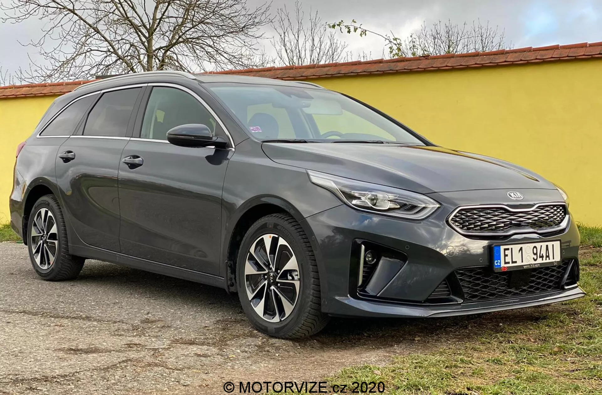 Bilden visar Kia Ceed 2018, en modern kombi fotograferad från en vinkel på trekvart framifrån, vilket framhäver dess front inklusive en strukturerad grill med ett distinkt varumärke emblem, smala svepande strålkastare med LED-dagsljus och en främre stötfångare med dimljus och parkeringssensorer. De eleganta konturerna av motorhuven leder till en brant lutande vindruta, vilket framhäver bilens aerodynamiska profil. Synliga är också fler-eikers lättmetallfälgar och sidospeglar med integrerade blinkers, tillsammans med en sluttande taklinje mot bakdelen och takräcken som betonar både stil och nytta. Tonade rutor och karosslinjer längs sidan tillför en skulpterad framtoning. Bilen står stilla på en plan yta utomhus.