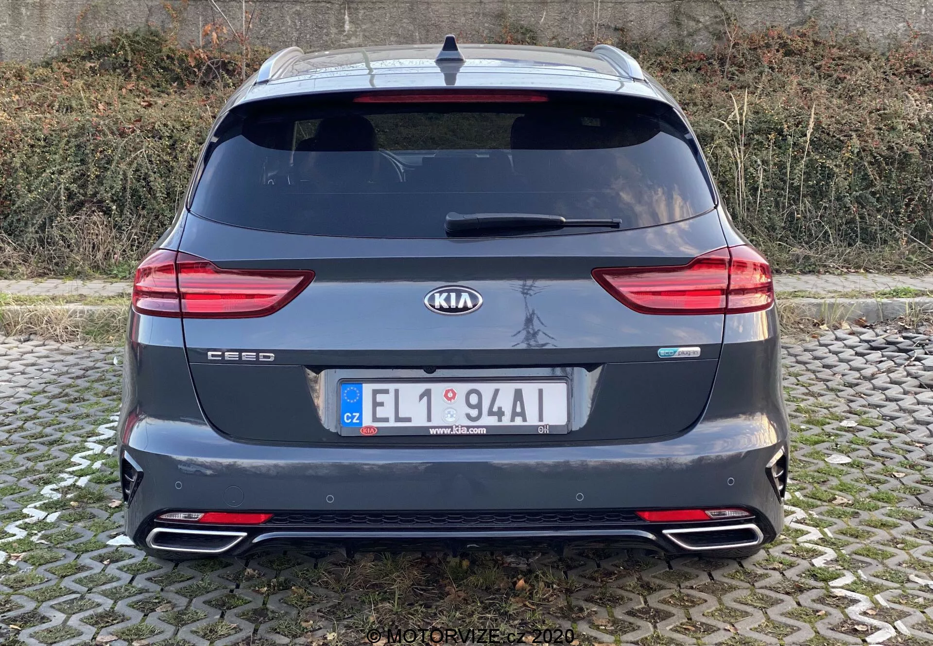 Bakifrån vy av en Kia Ceed 2018 som visar hela bakdelen med märke- och modellmärken, moderna LED-bakljus, bakruta, dubbla avgasrör, bakre stötfångare med reflexer, takspoiler, antenn och bakre parkeringssensorer. Bilden är klar, tagen från ögonhöjd med naturligt ljus under molniga förhållanden.