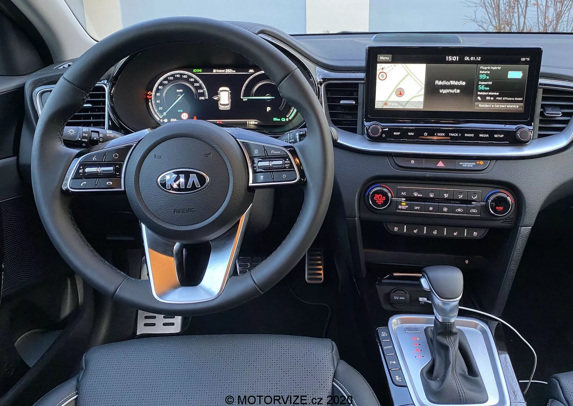 Interiörvy av en 2018 Kia Ceed från förarens perspektiv, som visar en treekrad ratt med Kia-logotyp, rattmonterade reglage, en kombinerad analog/digital instrumentbräda, en flytande infotainmentskärm med navigations- och mediegränssnitt, fysiska klimatkontroller och en automatisk växelspak med potentiell körlägesväljare eller elektronisk parkeringsbroms.