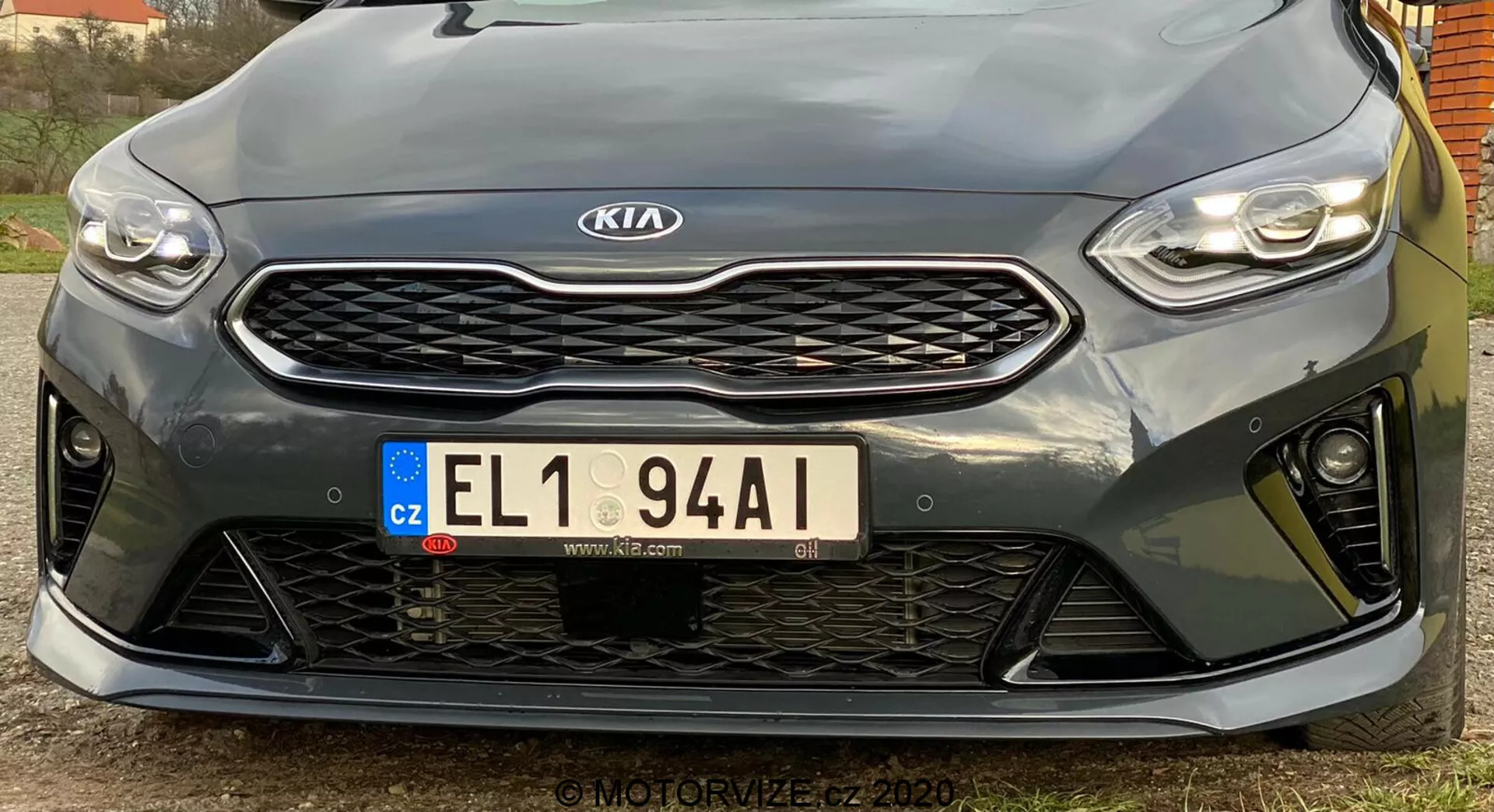 Denna bild visar fronten av en Kia Ceed 2018 sett från en låg vinkel. Den framhäver de eleganta, horisontellt orienterade LED-strålkastarna, den framträdande grillen med bikakemönster och en centrerad Kia-symbol, den europeiska registreringsskylten från Tjeckien och den sportiga främre stötfångaren med stora öppningar. Närbilden betonar parkeringssensorerna under grillen. Den sportiga designen tyder på en högpresterande trimnivå, även om exakta specifikationer är oklara. Den högupplösta bilden fångar designkritiker och konturer, med en något off-center vinkel till vänster.