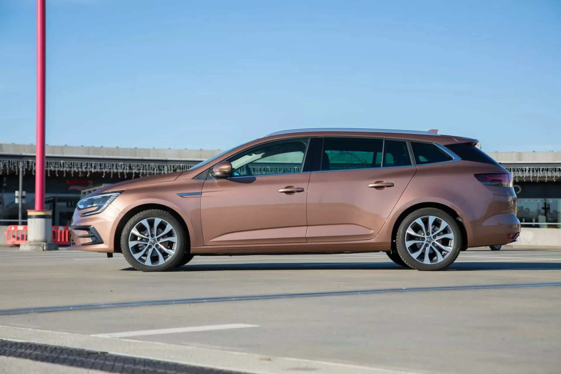 2009 Kia Ceed stationvagn i metallisk persikofärg, hel sidoprofilvy på mönstrat underlag, visar legeringshjul och elegant design under klarblå himmel