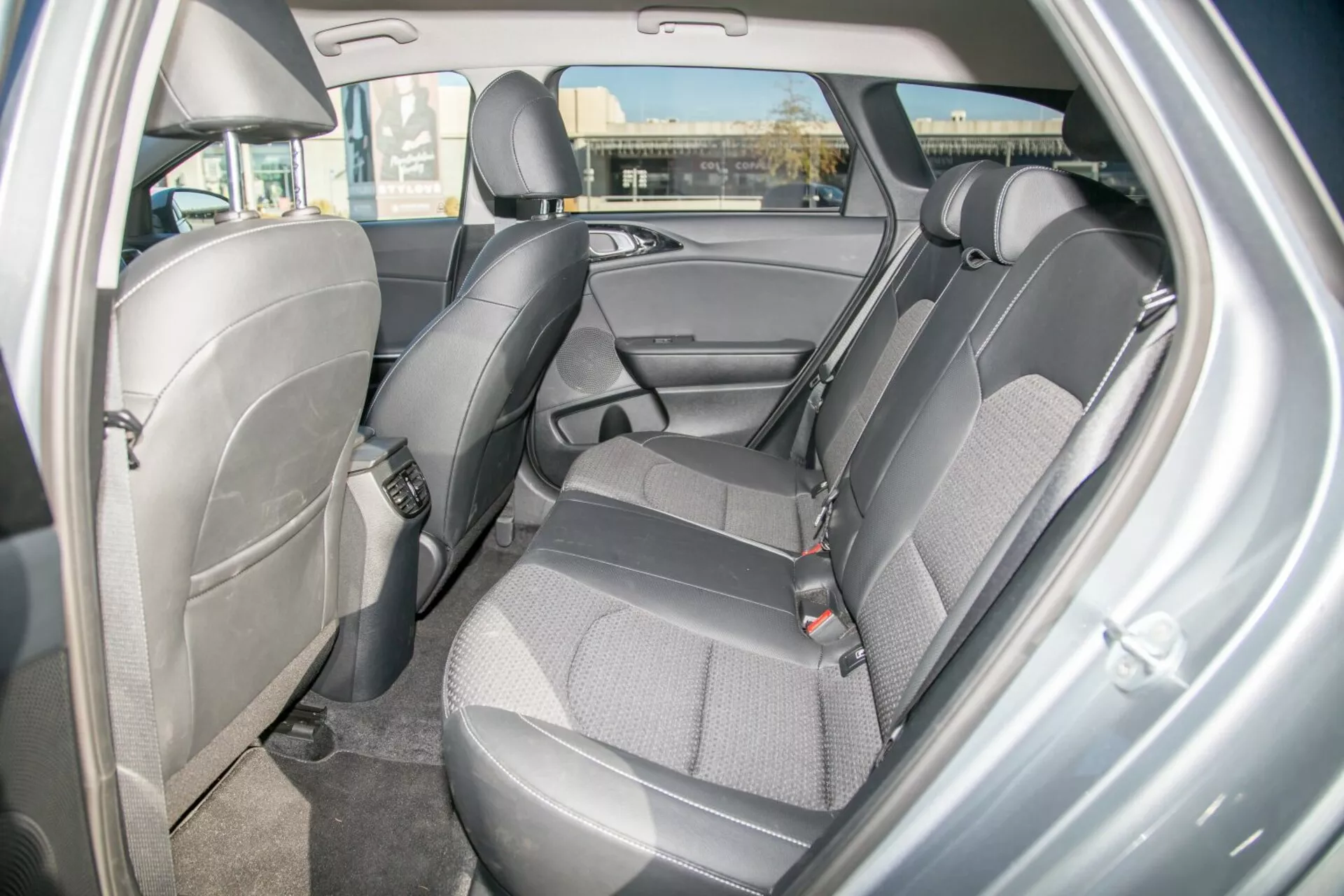 Interiörvy av en Kia Cee'd 2009 som visar designen och funktionerna i baksätets område, framhäver slitstark tvåtonig tygklädsel, synliga säkerhetsbälten, justerbara nackstöd, dörrpanel med förvaringsutrymme, potentiella barnsitsankare, mattat golv och omgivande kupébelysning från perspektivet av den högra sidans bakre passagerardörr.