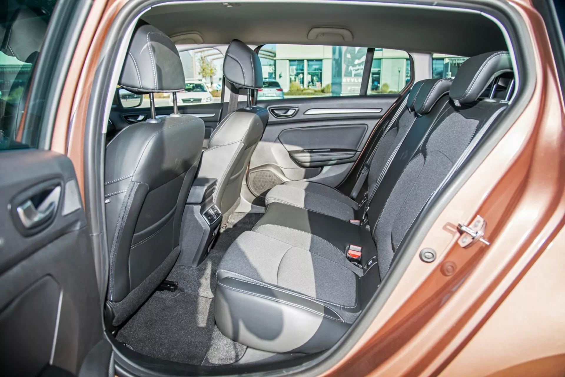 Interiör av Kia Ceed 2009 som visar den tvåfärgade bakbänken med ett säte fällt framåt för last, säkerhetsbälten, nackstöd, kontroller för elfönster och dörrhögtalare, vilket framhäver flexibel sittarrangemang och lyxig design
