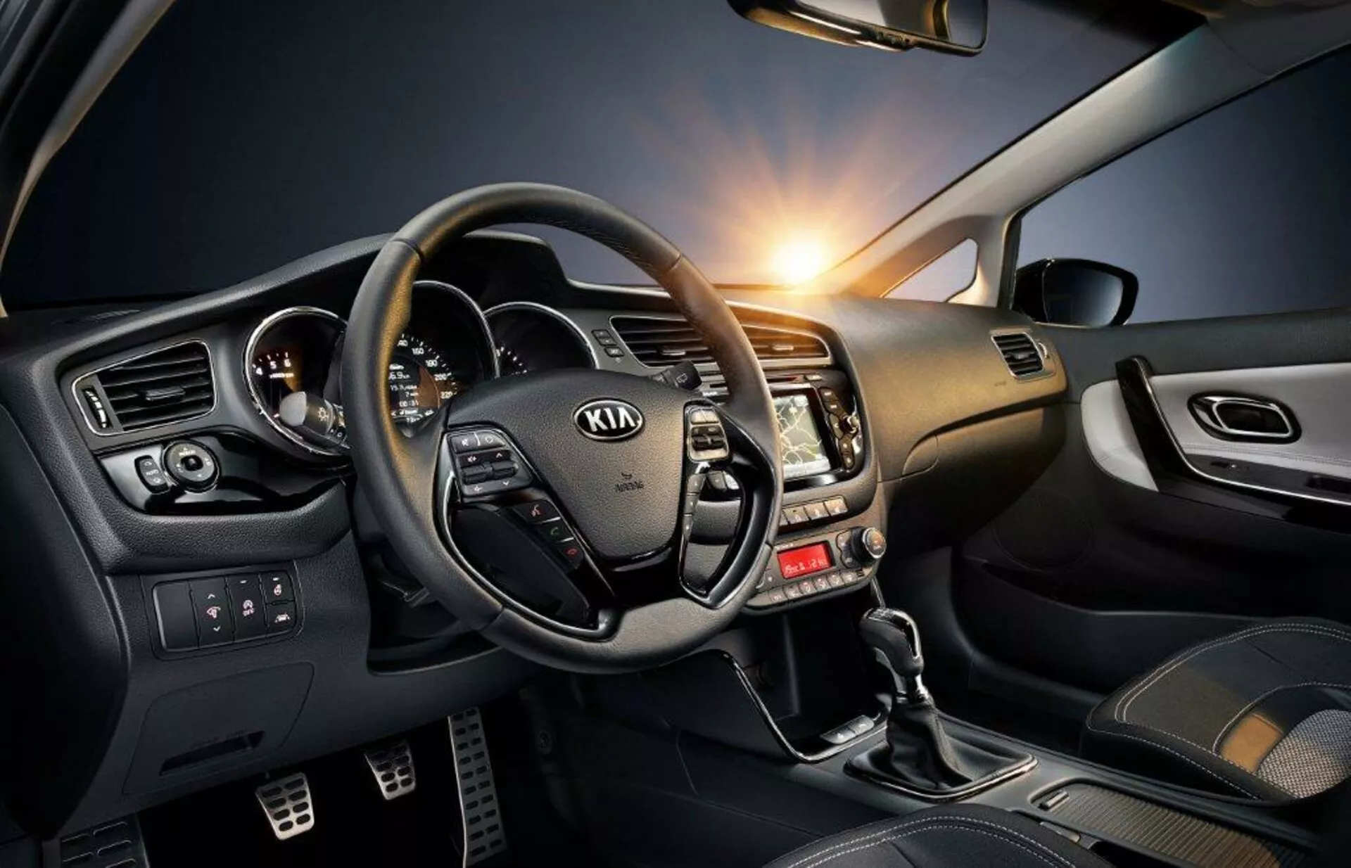 Interiör cockpitvy av en Kia Ceed 2009 som visar ratten med monterade kontroller, metallaccentuerad instrumentbräda och tekniktät förarsida inklusive växelspak, kontroller för elektriska fönster och omgivningsbelysning.