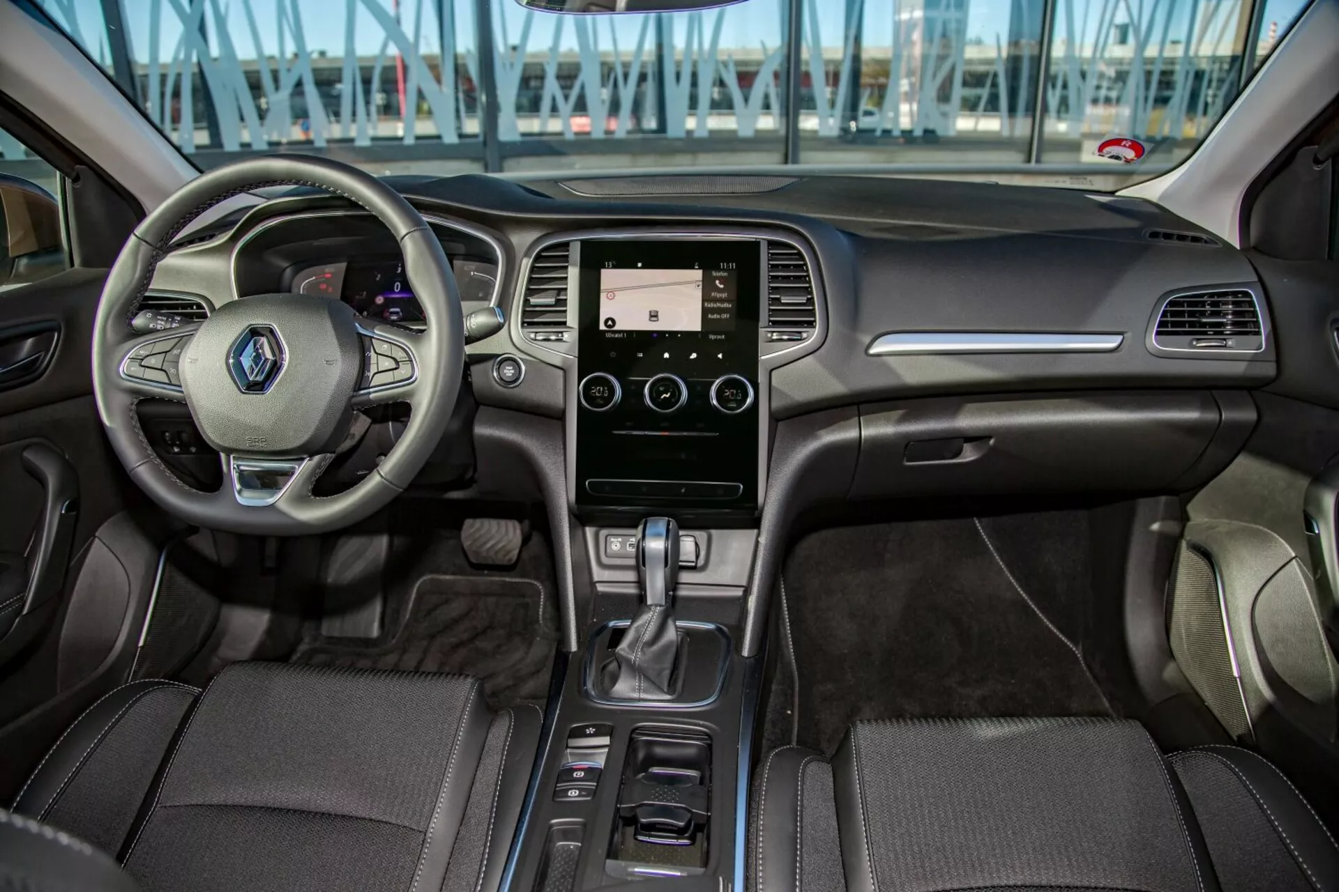 Interiörvy av Kia Cee'd 2009 från baksätet som visar multifunktionellt ratt, pekskärms infotainmentsystem, automatisk växelspak och detaljerad klädsel i främre cockpitområdet