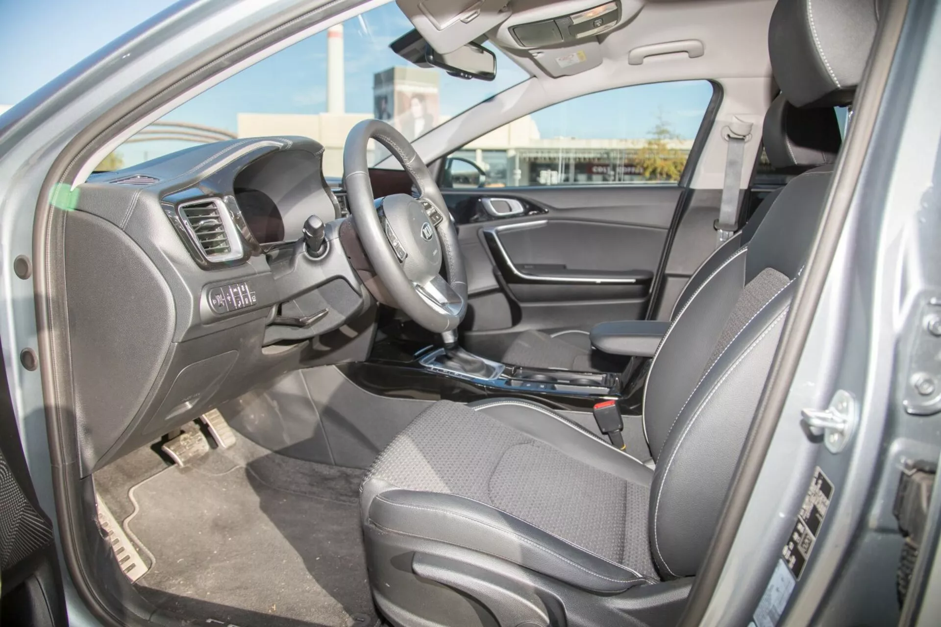 Interiörvy av Kia Cee'd 2009 från förarsidan som visar sätet, ratten med integrerade kontroller och funktioner på instrumentbrädan inklusive multimediasystem