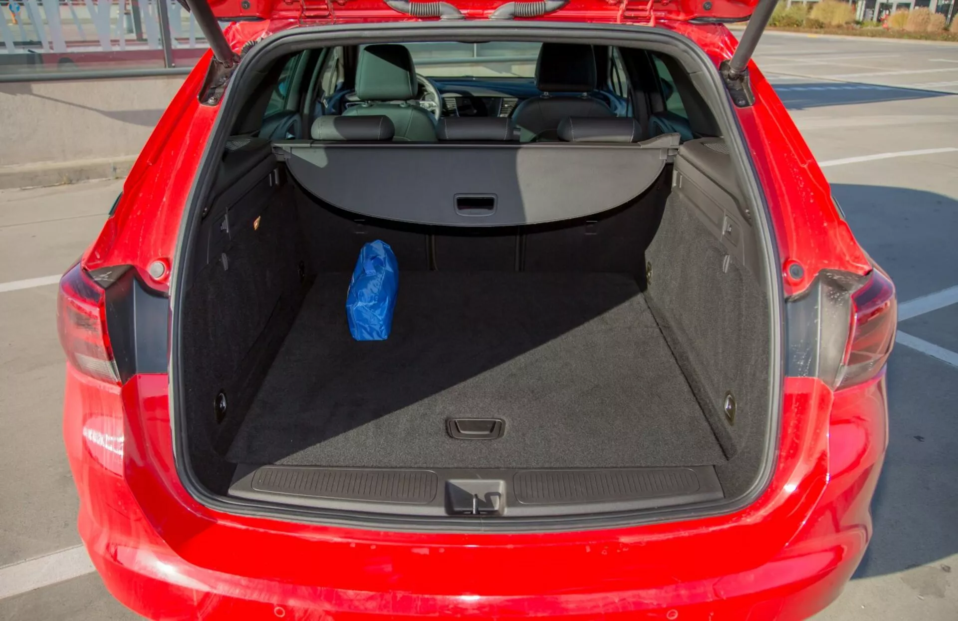Detaljerad vy av det öppna bagageutrymmet i en röd Kia Cee'd från 2009, som visar ett rymligt förvaringsutrymme och 60/40 delbara baksäten, med en blå väska som visar användbarheten.