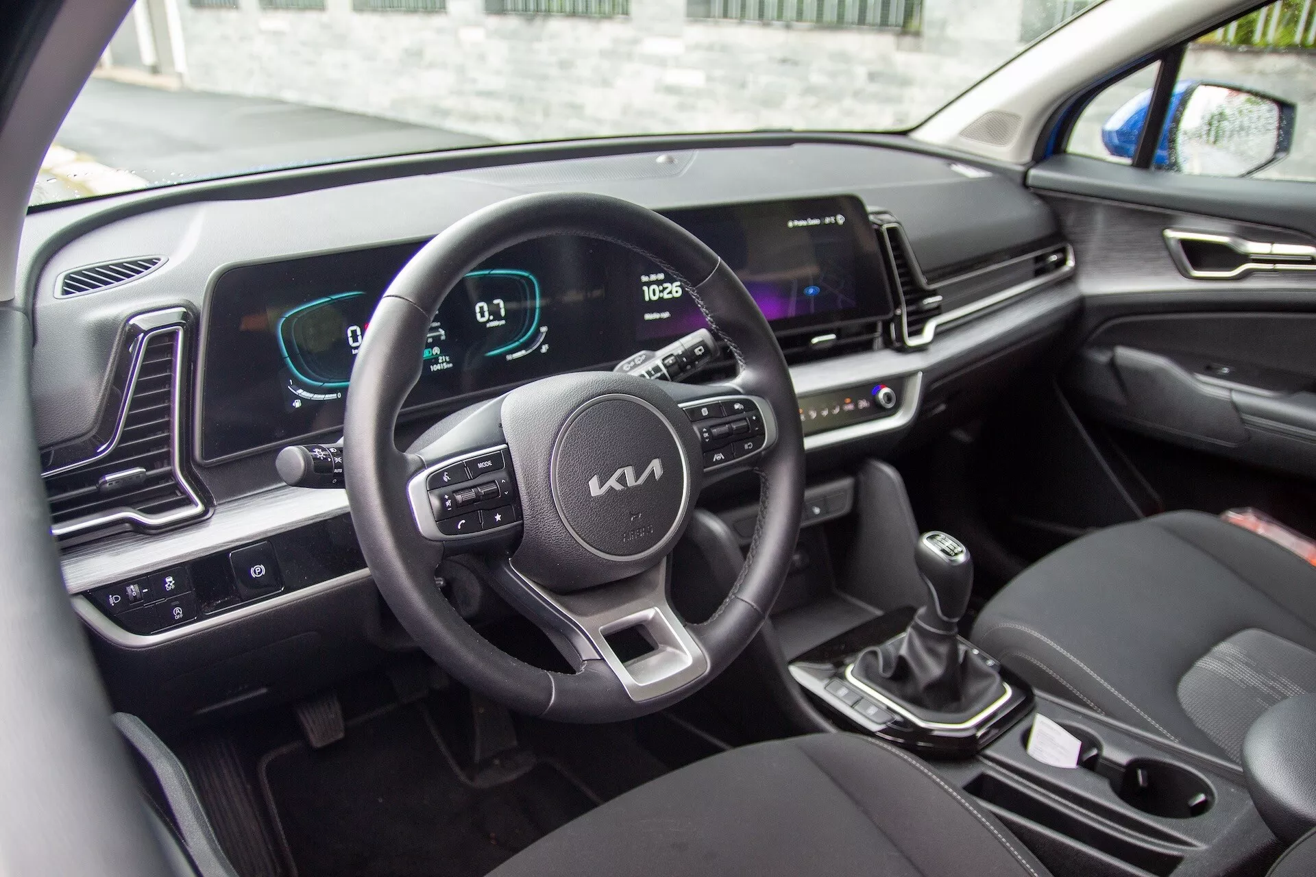 Interiör av Kia Sportage 2022 som visar ratten med kontrollknappar, digital instrumentpanel och infotainment-skärm
