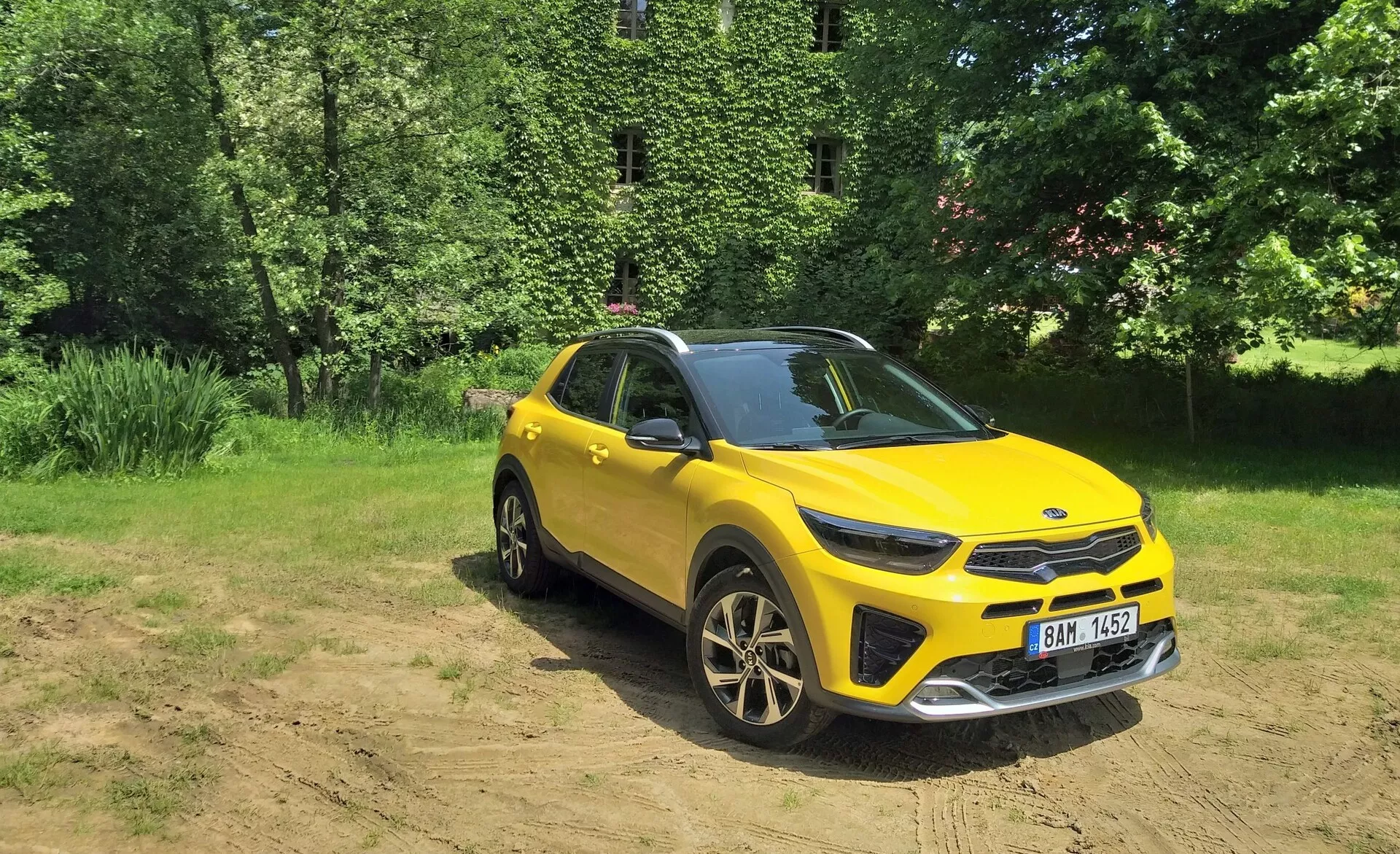Livligt gul crossover SUV Kia Stonic 2017 i en tre fjärdedels frontvy som framhäver dess frontgrill, LED-strålkastare, motorhuv och förarsida, placerad mot en naturlig bakgrund med solljus på klar mark, visar lätt terrängkörningsförmåga, sportiga lättmetallhjul och moderna designelement.