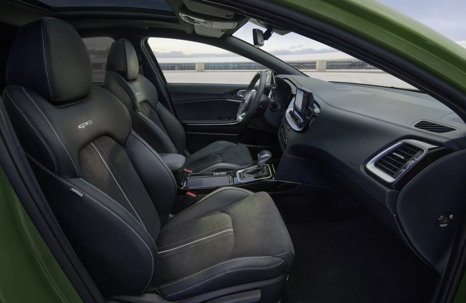 Interiörvy av Kia XCeed 2022 CD-facelift med sportiga svarta säten med kontrastsömmar, ett läderomslaget platt bottenrattpaket med multifunktionsstyrning, en slank instrumentbräda med en stor infotainmentskärm, ett digitalt instrumentkluster, en automatväxelspak, och förarsidans dörrkontroller, allt inkapslat i modern fordonsteknologi och lyxiga funktioner.