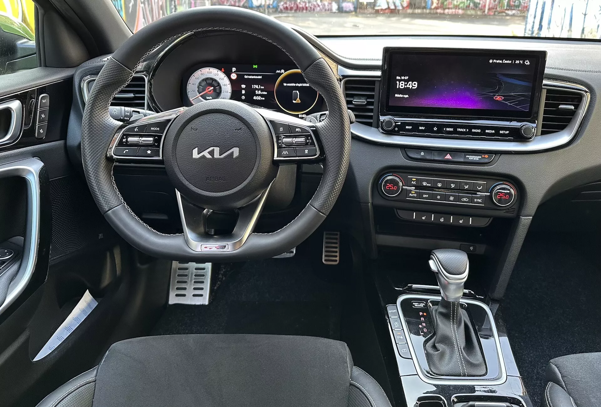 Interiörvy av Kia XCeed 2022 som framhäver förarcentrerade funktioner såsom en multifunktionell läderklädd ratt med knappar för multimedia och farthållare, en digital instrumentkluster, ett stort touchscreen-infotainmentsystem, automatisk klimatkontroll, automatisk växelspak, säten med tvåtonig klädsel och metall sportspedaler från ett första persons perspektiv.
