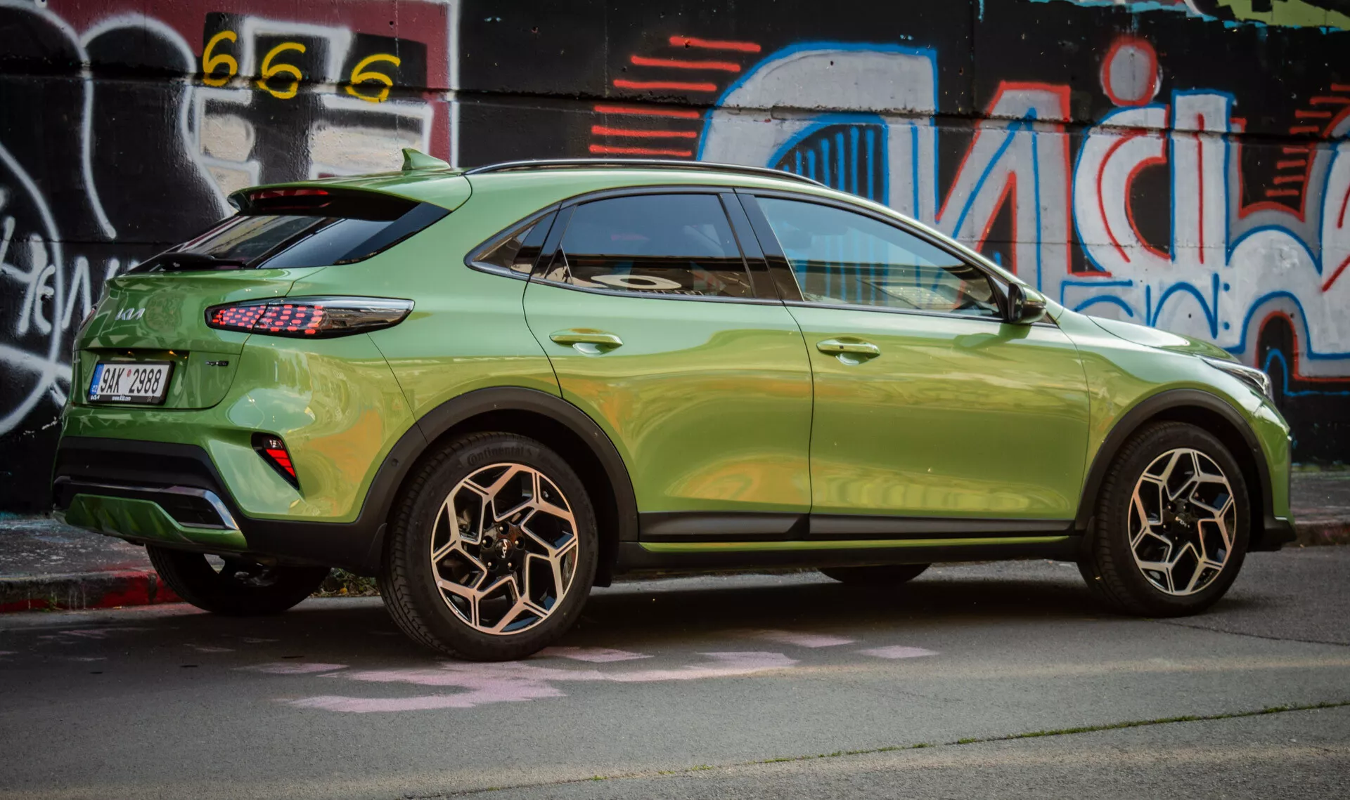Sidovy av Kia XCeed 2022 som framhäver designen på bakhjulet, metallisk grön färg, LED-bakljus och kompakt SUV-styling med aerodynamiska funktioner mot en bakgrund av urban gatukonst.