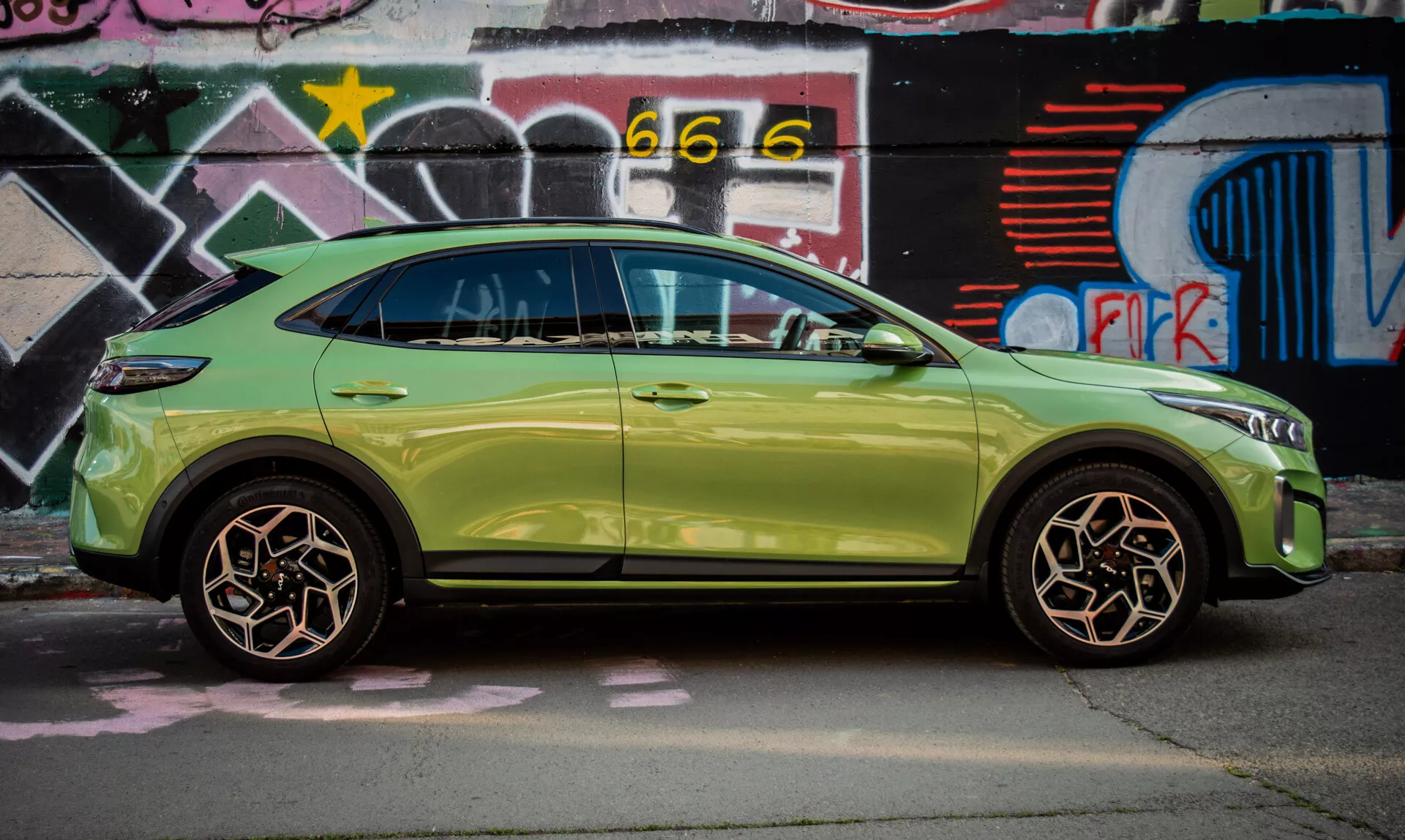 Kompakt SUV Kia XCeed 2022 i limegrönt parkerad vid en vägg täckt med graffiti, som visar upp sin slanka design och avancerade funktioner som nyckelfritt ingångssystem och integrerade blinkers i sidospelen.