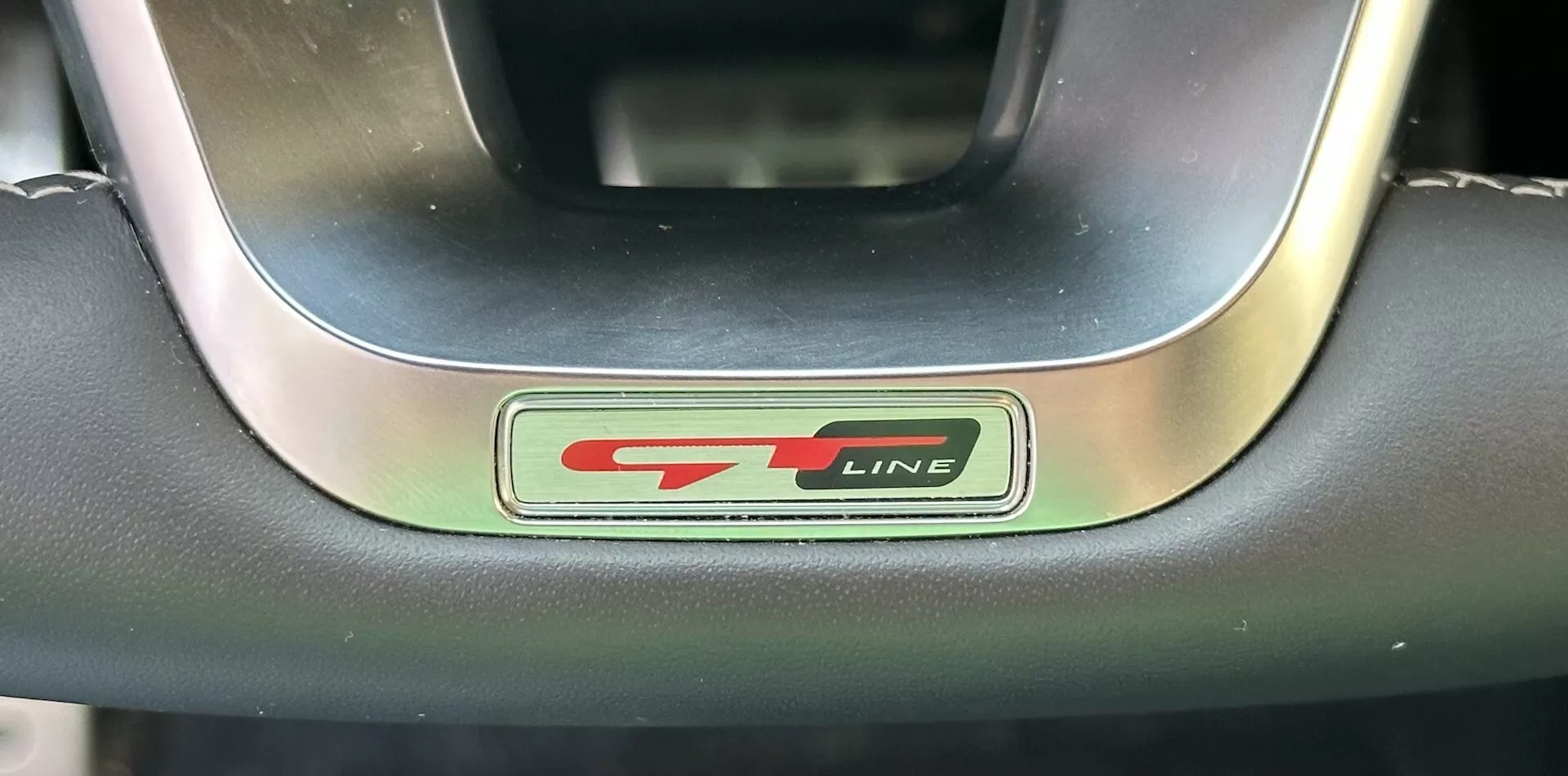 Närbild av Kia XCeed 2022 GT-Line-rattmärket som visar metalliska och svarta bokstäver med en sportig röd accent, omgiven av ett premium läder och metallratt