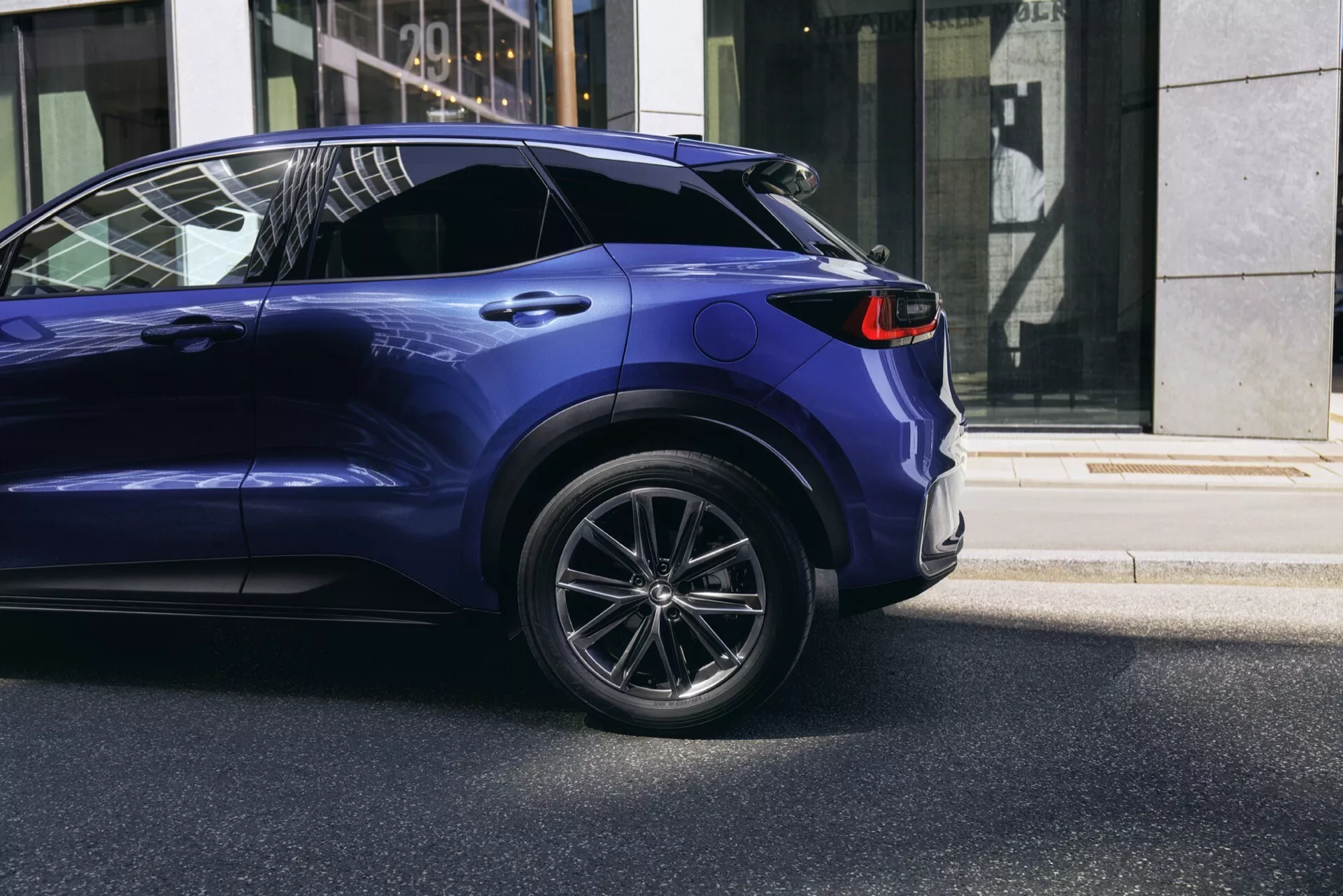 Bakre kvartsutsikt av Lexus LBX 2024 som visar legeringshjul, LED-bakljus och metalliskt blå målning på en stadsgata