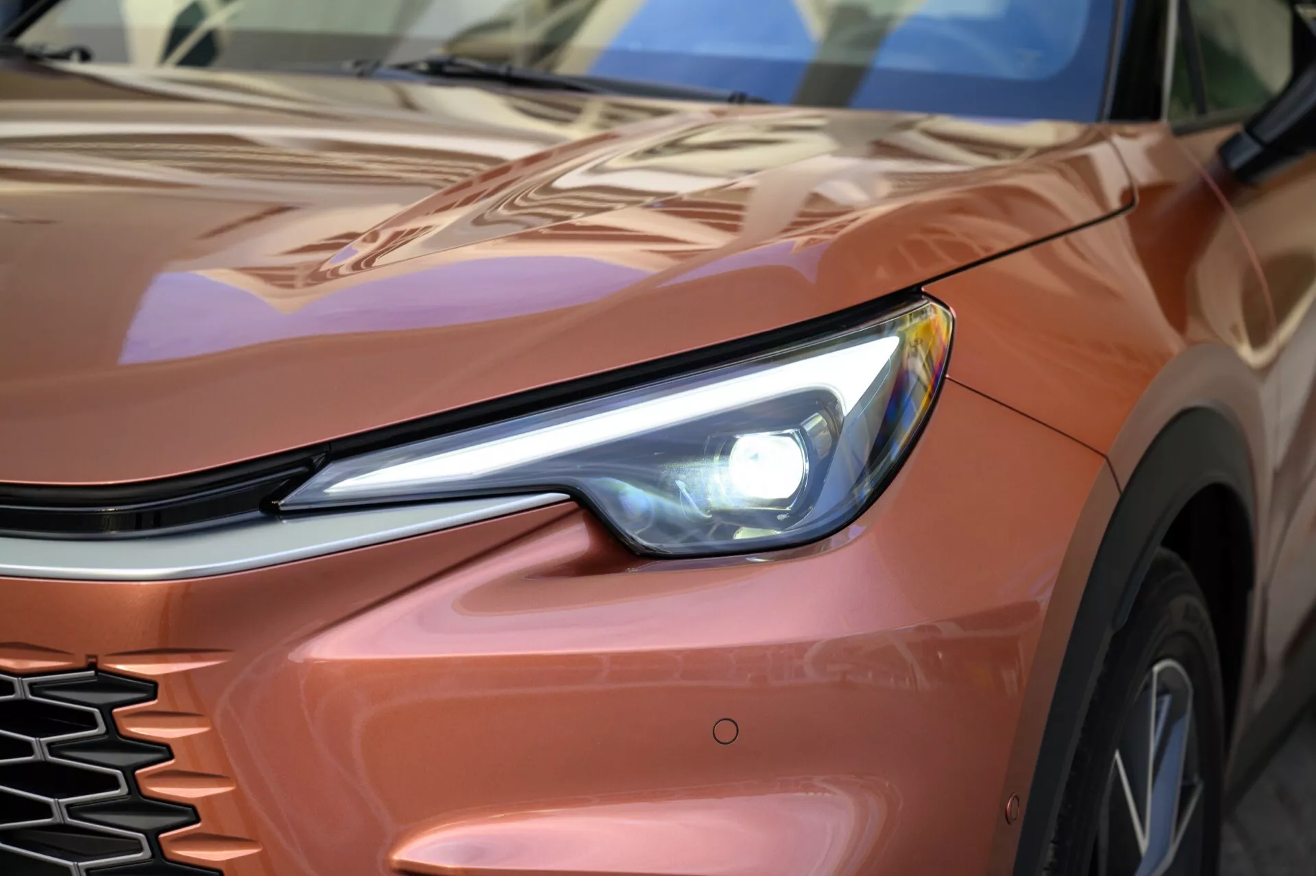 Närbild av en 2024 Lexus LBX, första generationen, fokuserad på den främre vänstra kvarten med detaljerad vy av LED-strålkastare, grill och konturerad huva och skärm från en låg vinkel, betonar dess slanka design och moderna teknologiska element.