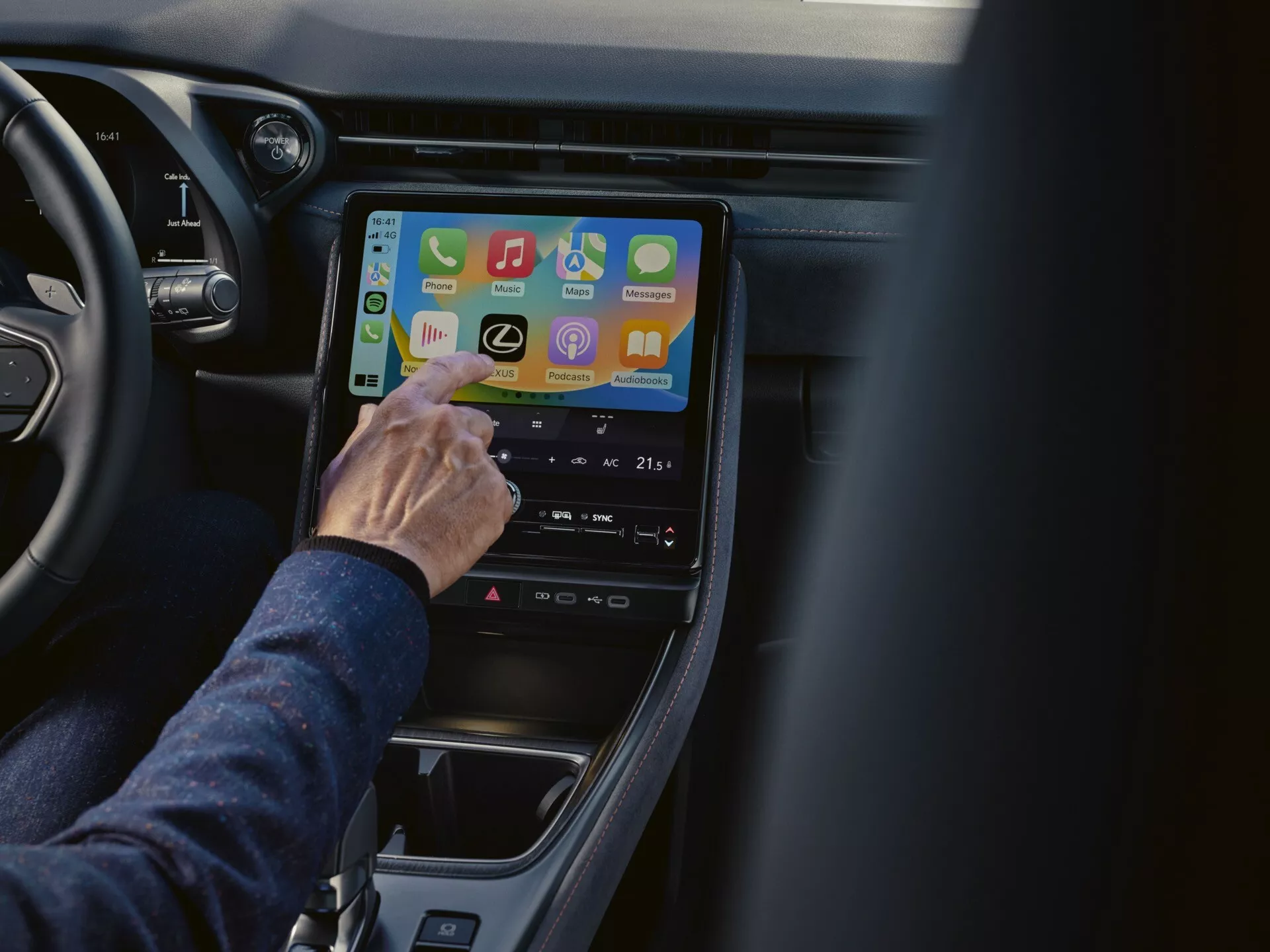 Närbild inuti en Lexus LBX 2024 med fokus på infotainmentsystemet ur passagerarens perspektiv, visar anslutningsappar och inställningar för klimatkontroll på en vertikalt placerad pekskärm