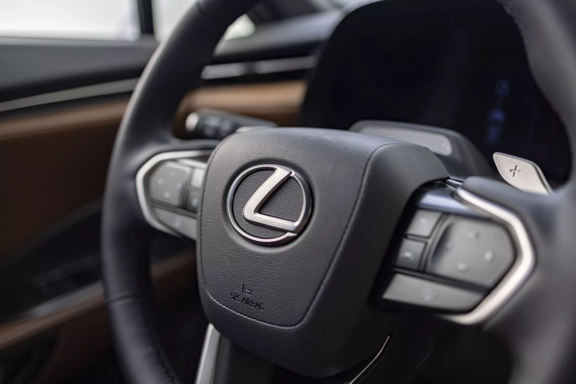 Närbild av ratten på Lexus LBX 2024 med fokus på Lexus-logotypen och kontrollknappar, betonar lyx och avancerad teknik