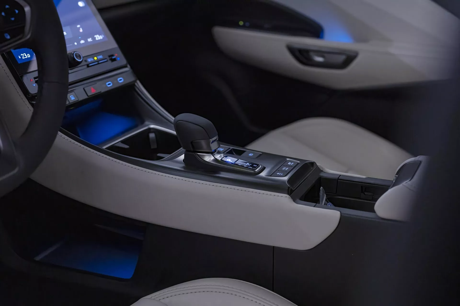 Interiör av Lexus LBX 1:a Generationen 2024 med översikt över mittkonsolen och den automatiska växelväljaren med omgivningsbelysning, omgiven av en högteknologisk pekskärmspanel och detaljer i lyxigt krämigt läder