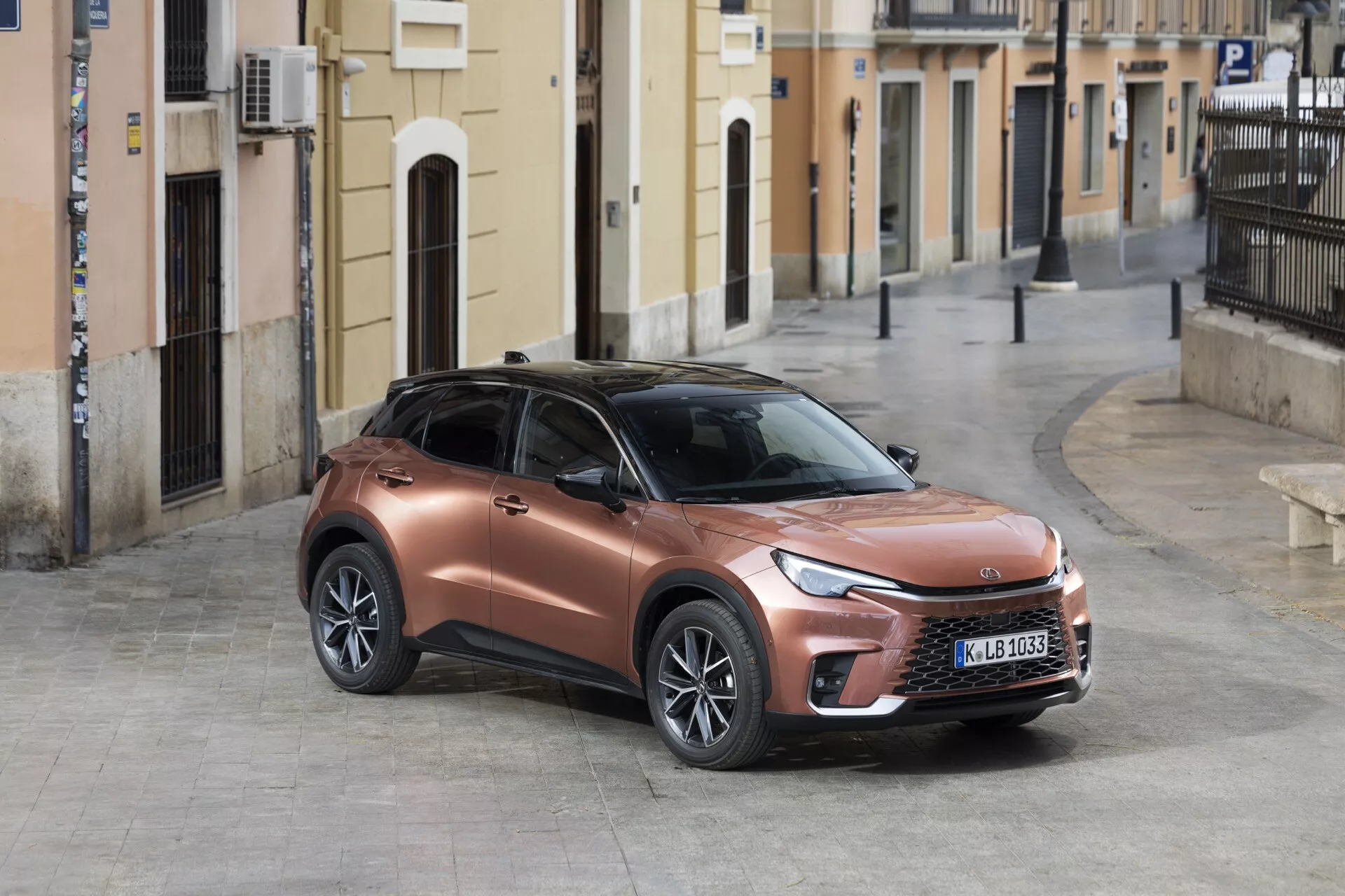 2024 Lexus LBX 1: a generationens moderna crossover-SUV parkerad på en kullerstensgata med en tre fjärdedelars främre vänstersida som visar upp dess metalliska bronsfinish, slanka LED-strålkastare och sportig, hög åkturdesign