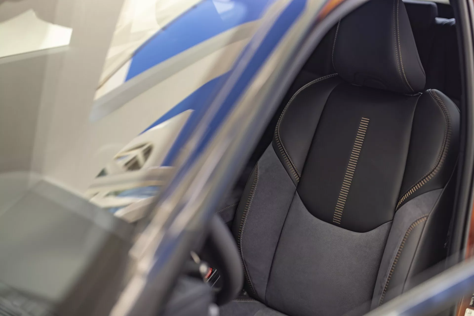 Närbild på förarsätet i Lexus LBX första generationen 2024 med högkvalitativt mörkt materialöverdrag med detaljerad sömnad och sportigt sidostöd, sedd genom en öppen dörr med fokus på ergonomiska funktioner och möjliga kontroller för elektrisk sätesjustering.