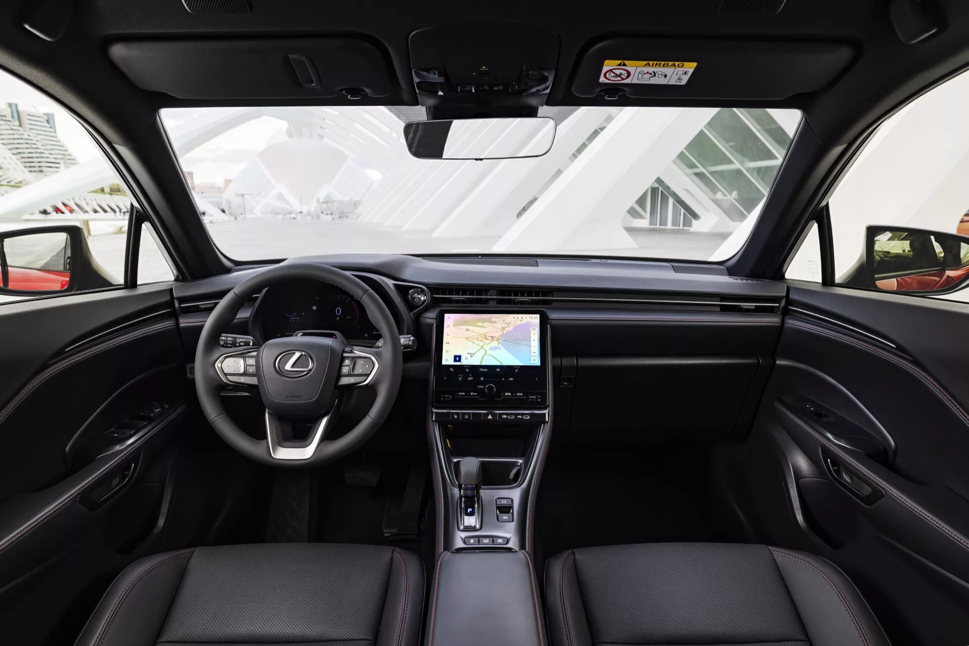 Interiörvy av Lexus LBX 1:a generationen 2024 från mitten av baksätet som visar instrumentbrädan, ratten, läderframsäten och högteknologiska funktioner