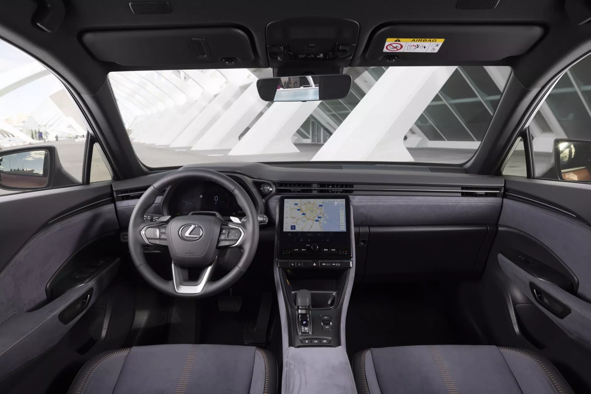 Interiörvy av Lexus LBX 2024 som visar instrumentbräda, ratt med Lexus-logotyp och inbyggda kontroller, pekskärmscenterkonsol, lyxiga sittplatser och avancerade teknikfunktioner från baksätets perspektiv