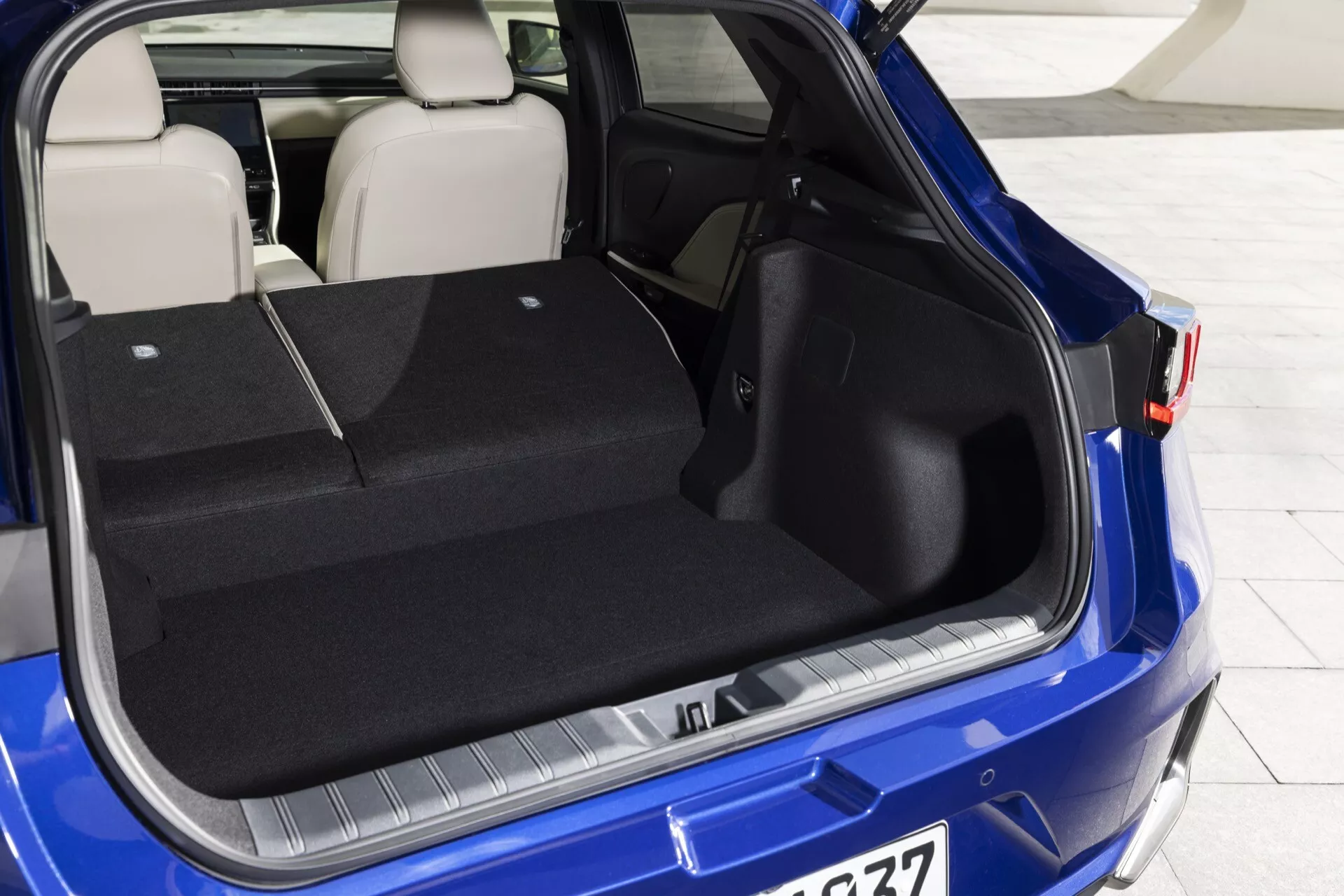 Vy av 2024 Lexus LBX 1:a generationens bagageutrymme med bakluckan öppen, visar rymligt lastutrymme, skyddstrim på stötfångaren, delbart bakre sätesdesign i en levande blå färg
