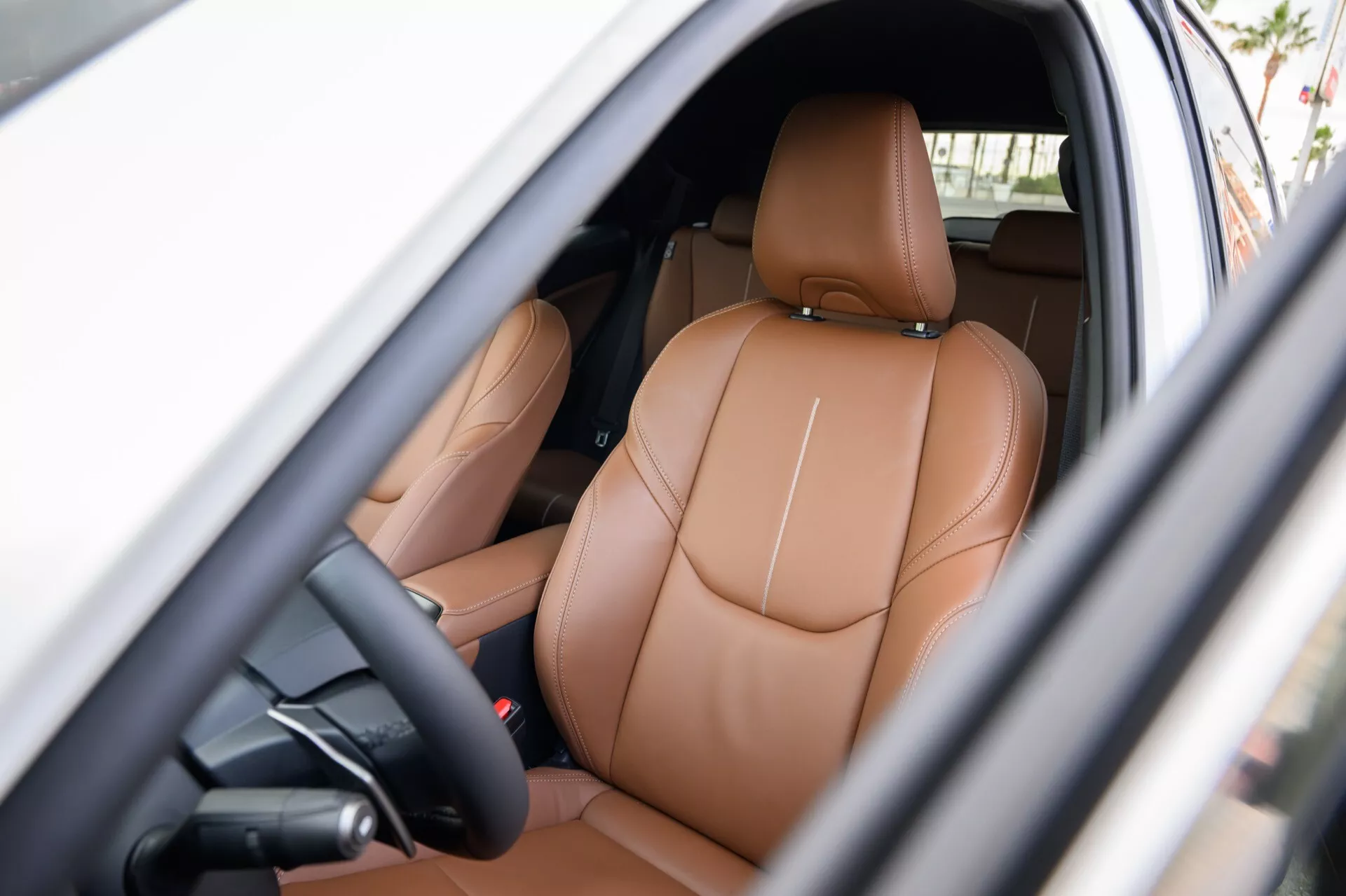 Interiörvy av en Lexus LBX 2024 1:a generation som visar förarområdet med lyxiga ljusbruna lädersäten, kraftjusteringskontroller och antydningar till högteknologiska funktioner synliga genom förarsidan öppna dörren