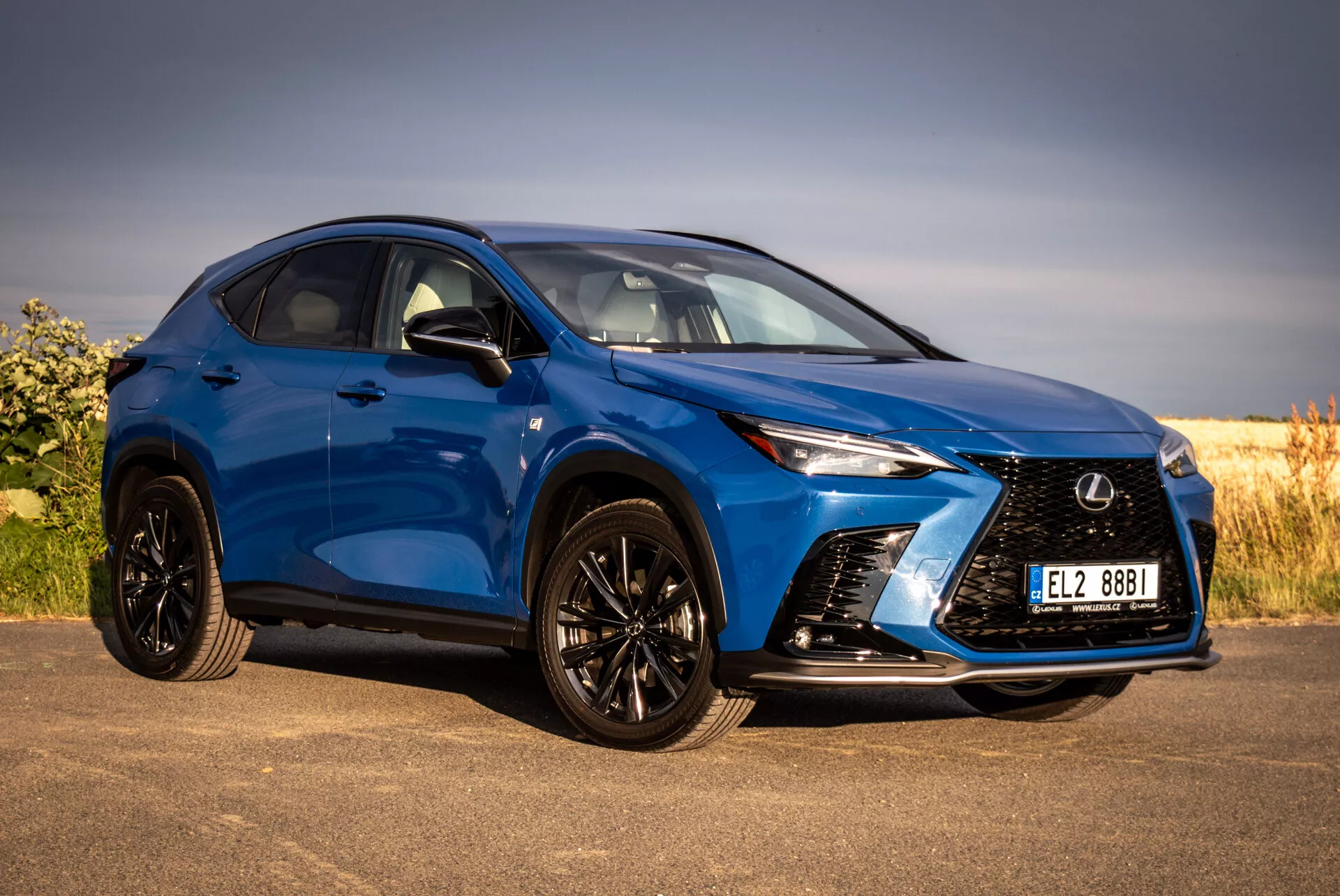 Blå SUV Lexus NX 2021 i främre tre fjärdedelars vy som framhäver dess aggressiva grill, skarpa LED-strålkastare, svarta lättmetallfälgar med lågprofildäck och karossfärgade sidospeglar mot en naturlig bakgrund