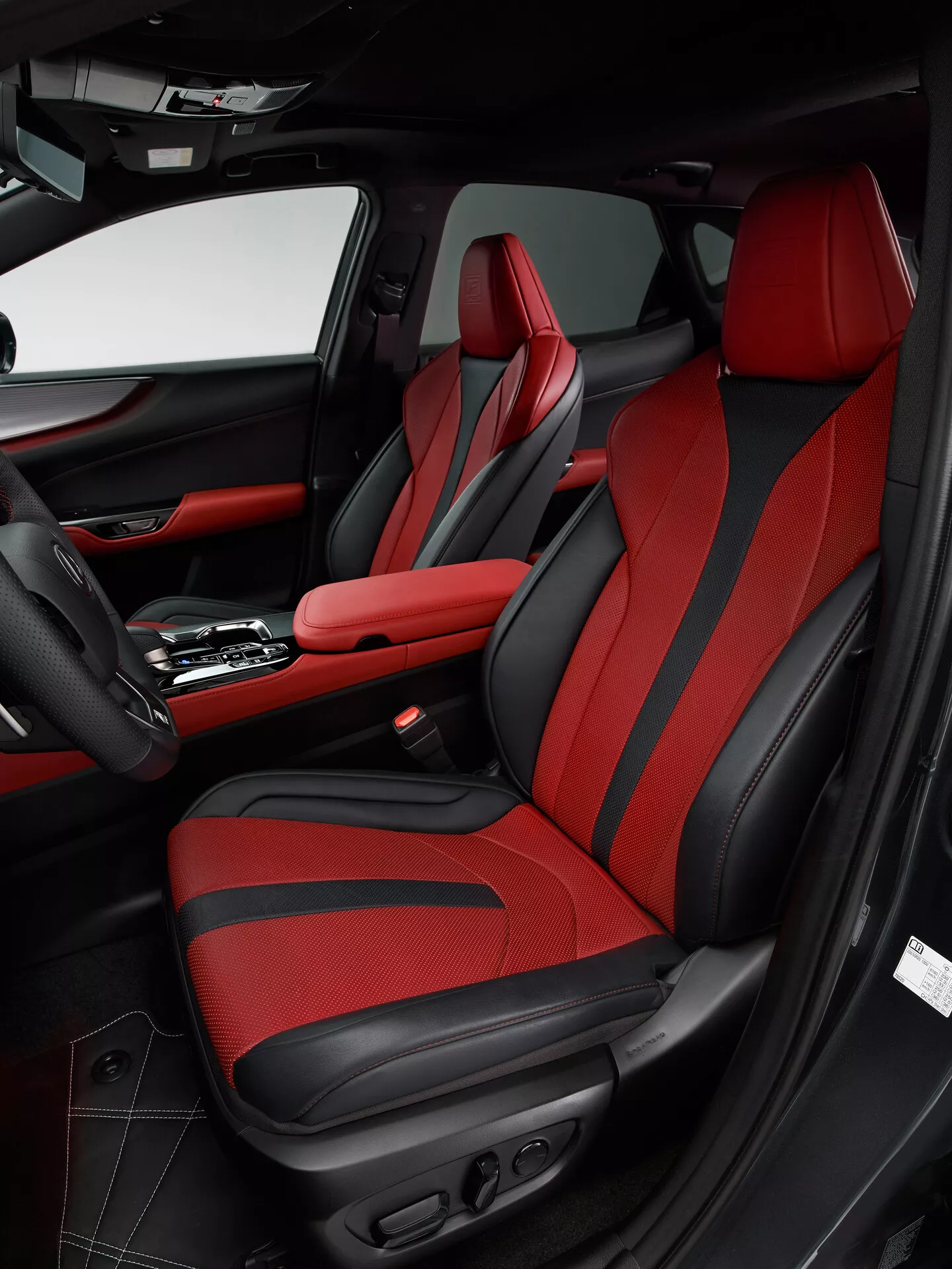 Interiörbild av en 2021 Lexus NX som visar passagerarområdet framifrån från förarens sida. Bilden betonar passagerarsätet med djärv röd klädsel och svarta accenter, med en sportdesign med förbättrat sidostöd och eljusteringar. Dörrpanelen matchar det svart-röda färgschemat och innehåller läder, tyg, en förvaringsficka, en högtalargaller och olika kontroller. Mittkonsolen visar en automatisk växelspak och ett centralt armstöd med röda sömmar, vilket speglar bilens lyxiga och sportiga design.