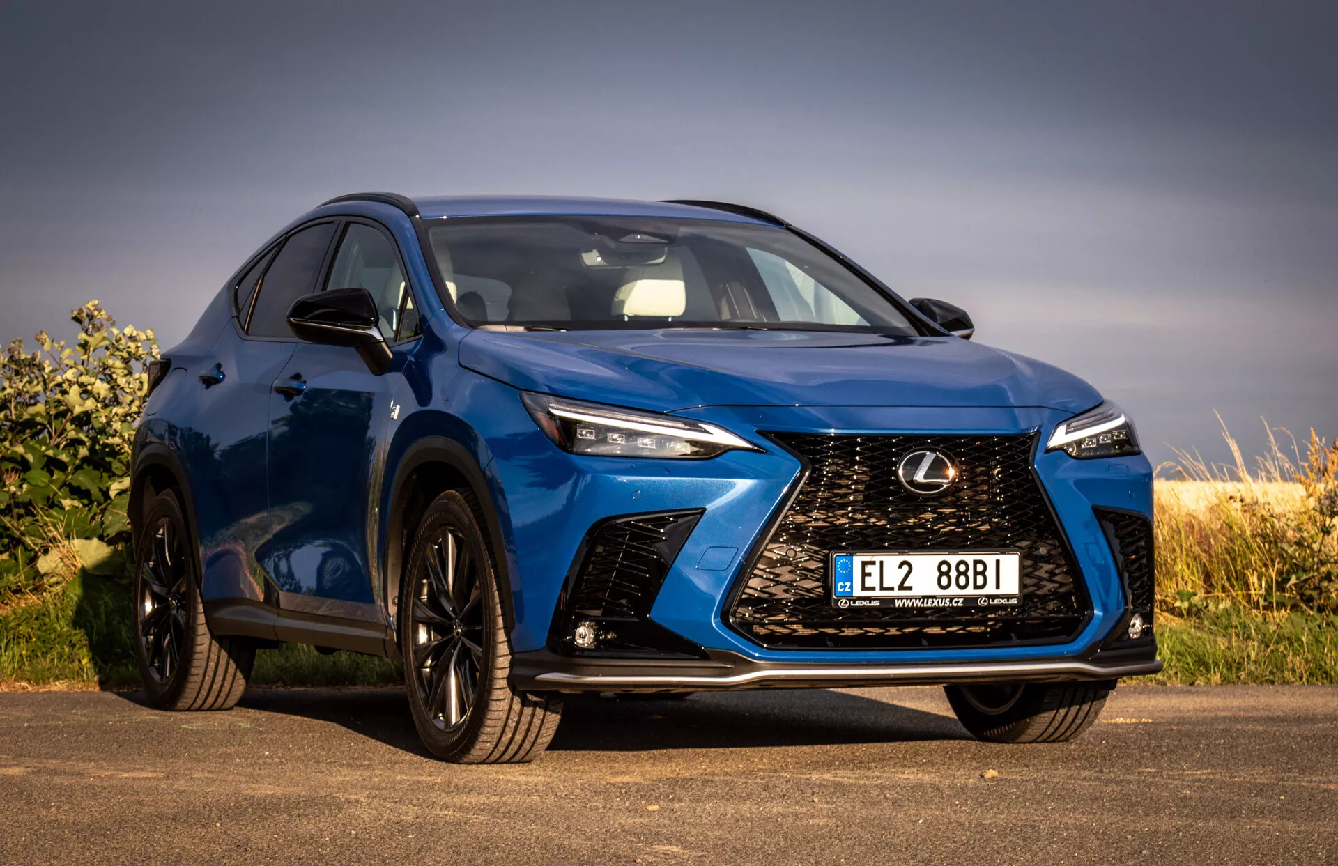 Lågvinkelskott av en blå Lexus NX SUV från 2021 som visar den främre grillen med spindeldesign, LED-strålkastare, svarta legeringshjul och integrerade blinkers på sidanspegeln, vilket betonar dess lyx- och prestandafunktioner.