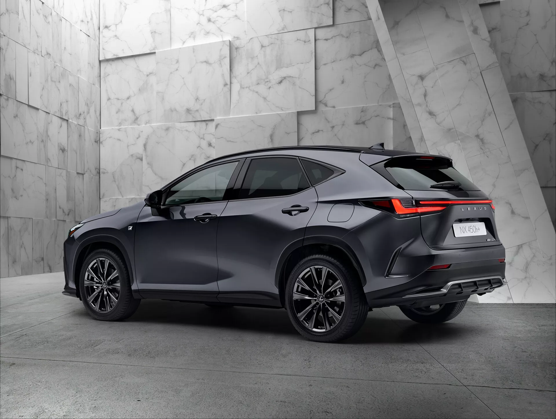 Trekvarts bakåtvänd vy av en modern 2021 Lexus NX SUV i en utställningsmiljö. Fordonets högra sida och bakdel syns tydligt, med bakljusen i en vinklad LED-design, mörk blank färg, flerspokedesignade hjul och taklinje med eventuella takräcken. Den neutrala, texturerade bakgrunden kontrasterar väl med SUV:ens sofistikerade design.