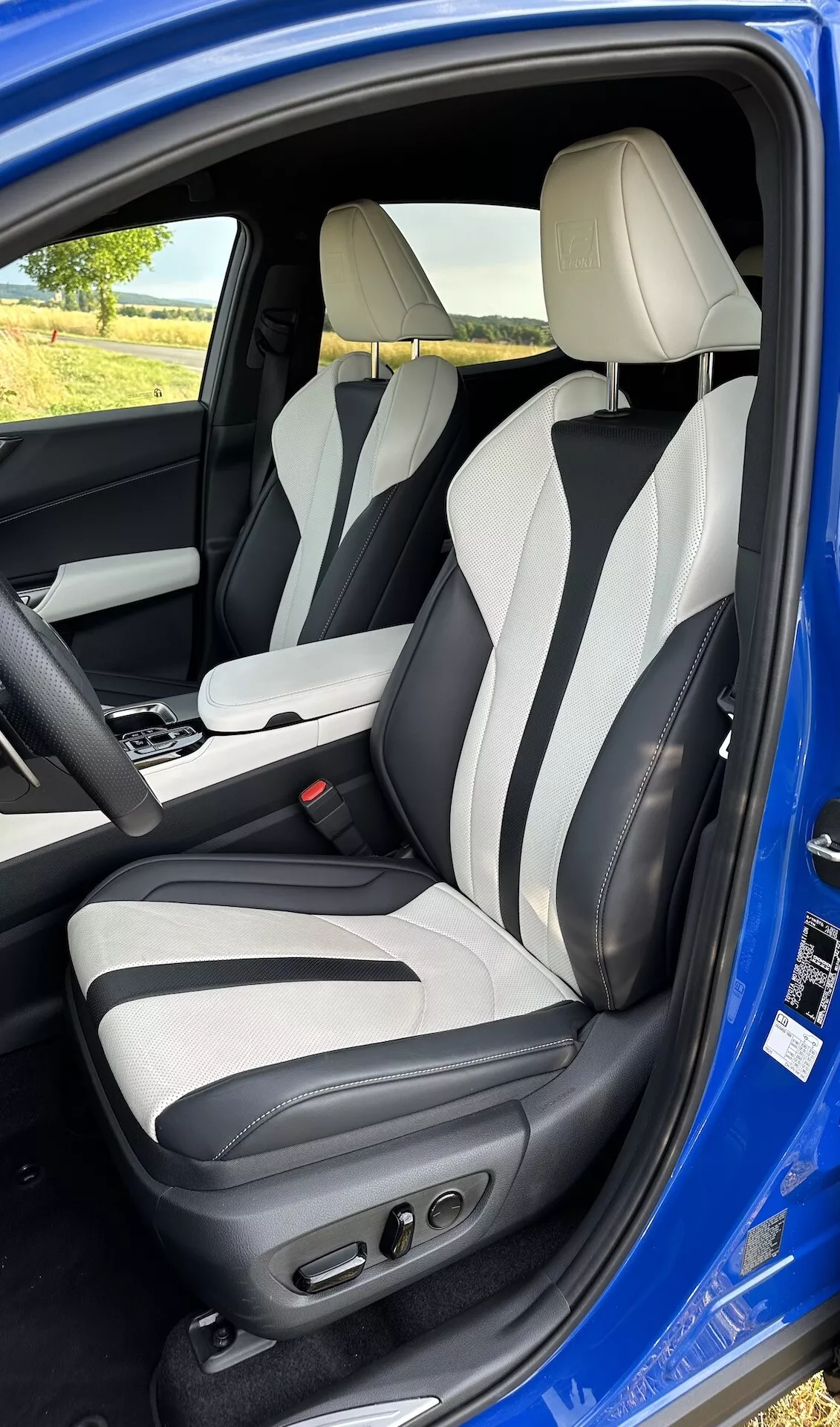 Interiörvy genom öppen förardörr på en Lexus NX 2021, som visar förarområdet från en lätt höjd, med tvåfärgad läderklädsel, avancerade förarsäteskontroller, sidostöd, integrerade nackstöd och mittkonsol med automatisk växelspak