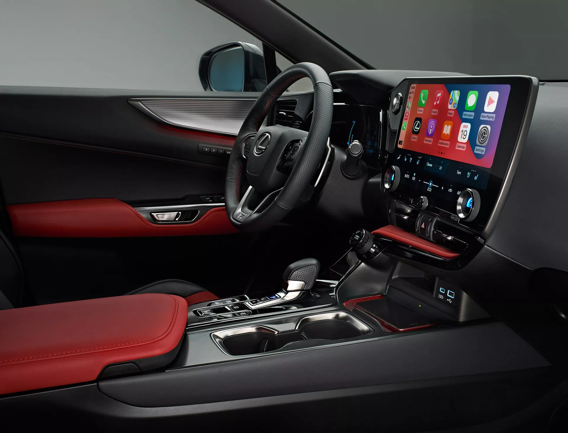 Interiörvy av 2021 års Lexus NX som visar förarsidan. Bilden fångar den multifunktionella ratten med monterade kontroller, en delvis synlig instrumentpanel och en framträdande mittkonsol med en stor, vertikalt orienterad infotainmentskärm som troligen visar Apple CarPlay. Under skärmen finns knappar för tvåzonsklimatanläggning. Växelspaken för automatlådan, material och design detaljer som svarta ytor med röda accenter på säten och dörrpaneler, samt en delvis vy av kontroller på förardörrens panel speglar fordonets sportiga och premiumkaraktär.