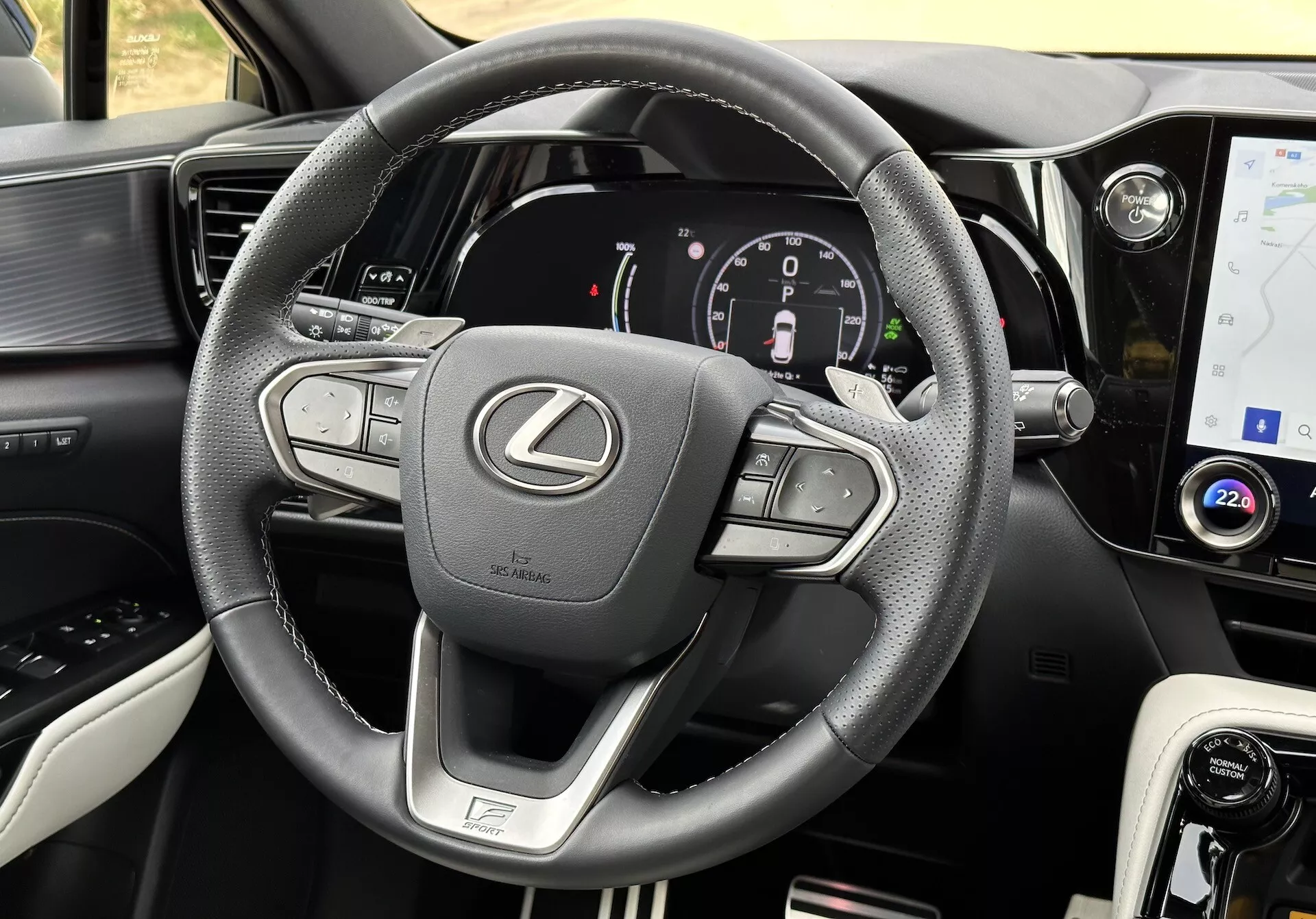 Interiörvy av en Lexus NX 2021 med fokus på ratten och instrumentbrädan, som visar multifunktionsknappar, en digital instrumentkluster, en infotainment pekskärm, läderaccent, en körmodusväljare, luftventiler och detaljerad sömnad.
