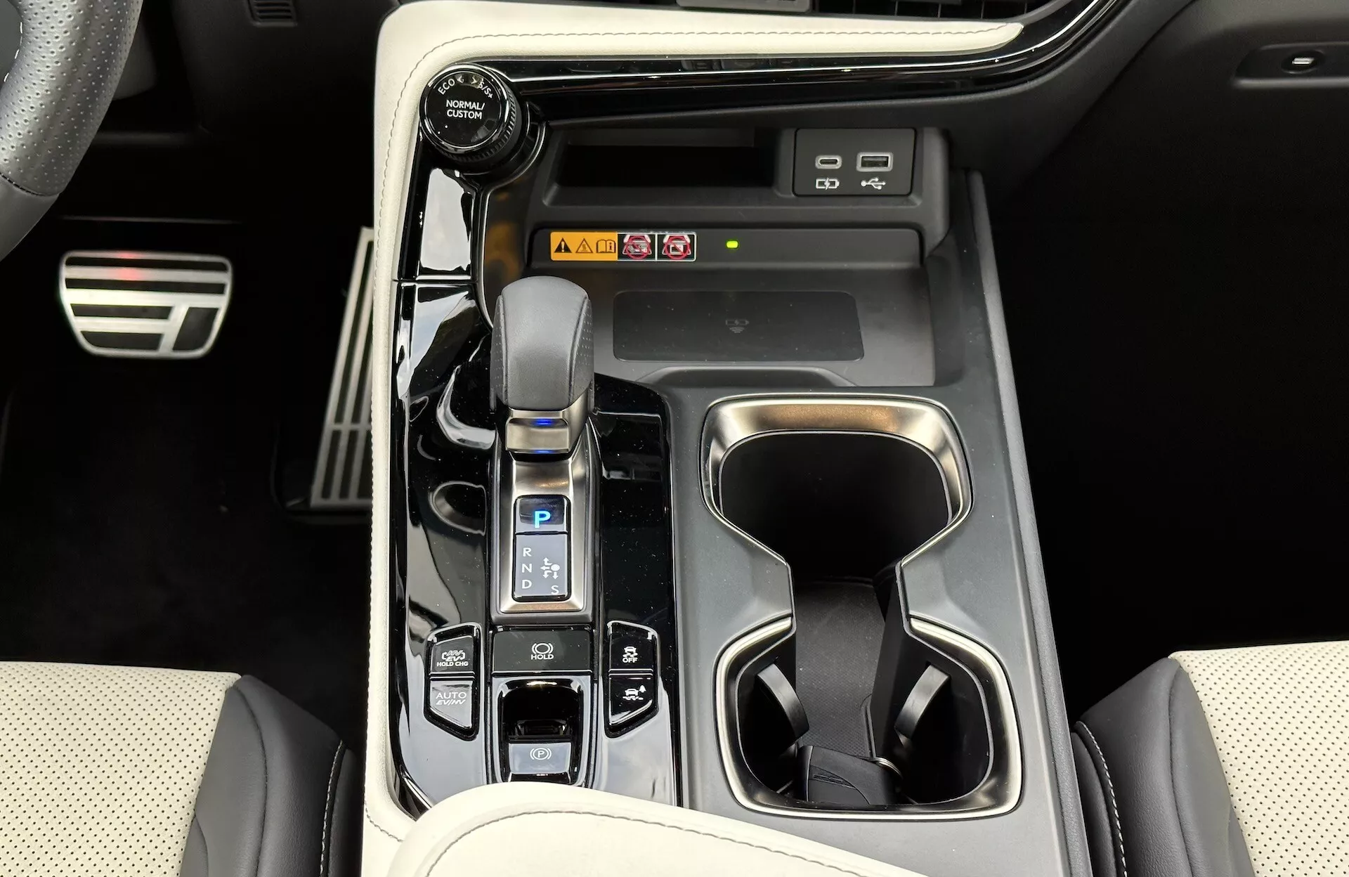 Vy av Lexus NX 2021 mittkonsol som visar automatisk växelspak med läderstövel, körlägesväljare, mugghållare, fordonets kontrollknappar, potentiella genvägar till infotainmentsystemet och lyxiga interiördesignelement