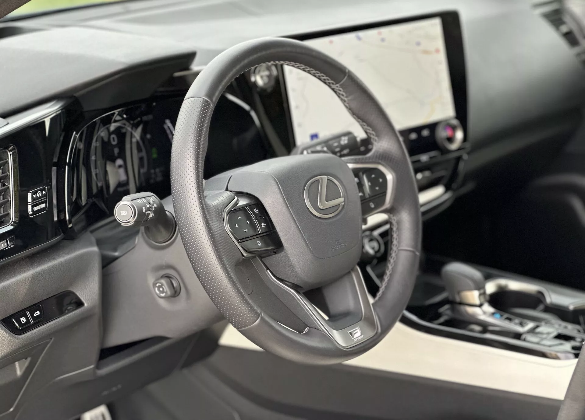 Interiörvy av Lexus NX 2021 med fokus på det läderklädda ratten med monterade kontroller och digital instrumentpanel bakom den, med stor infotainment-pekskärm och subtila antydningar av lyx i materialen av hög kvalitet