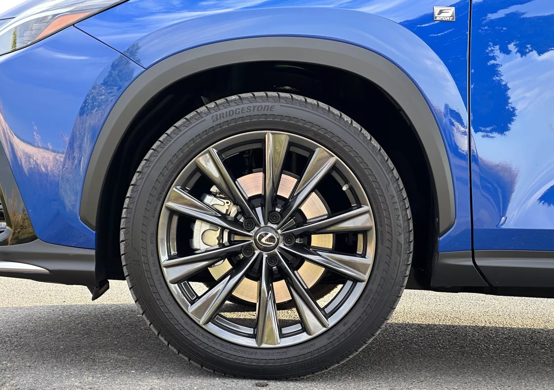 Detaljerad vy av 2021 Lexus NX passagerarsidan främre hjulet med en flerspakig design med två-ton finish och Bridgestone däck, mot en livlig blå kaross