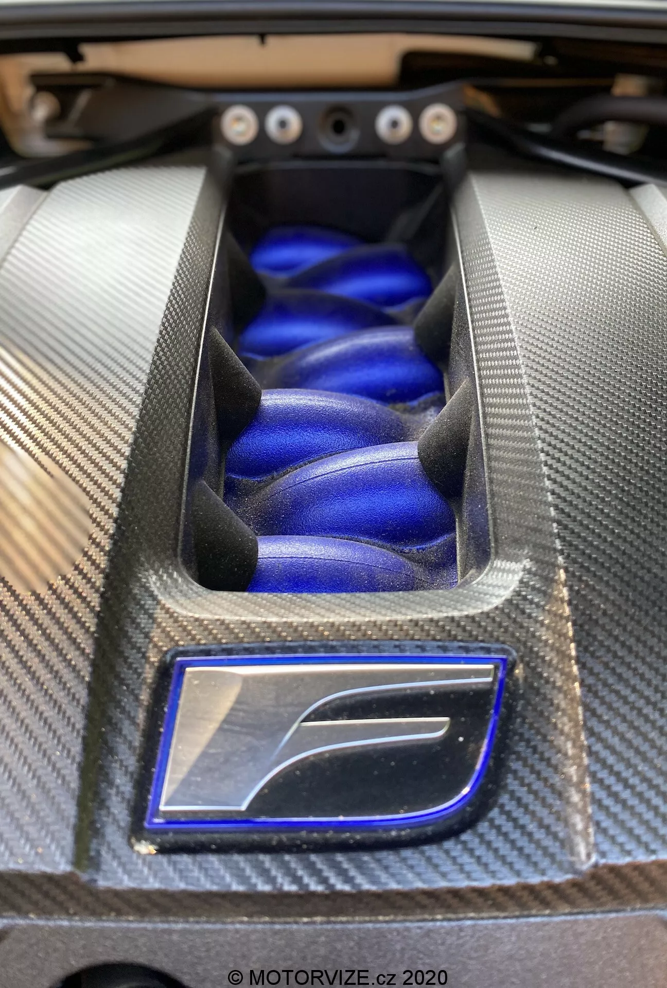 Närbild av motorutrymmet för prestandabilen Lexus RC 2016, med fokus på ett stiliserat motorlock med en strukturerad kolfiberram och en livfull blå finish, som exemplifierar högkvalitativ fordonsingenjörskonst och design.