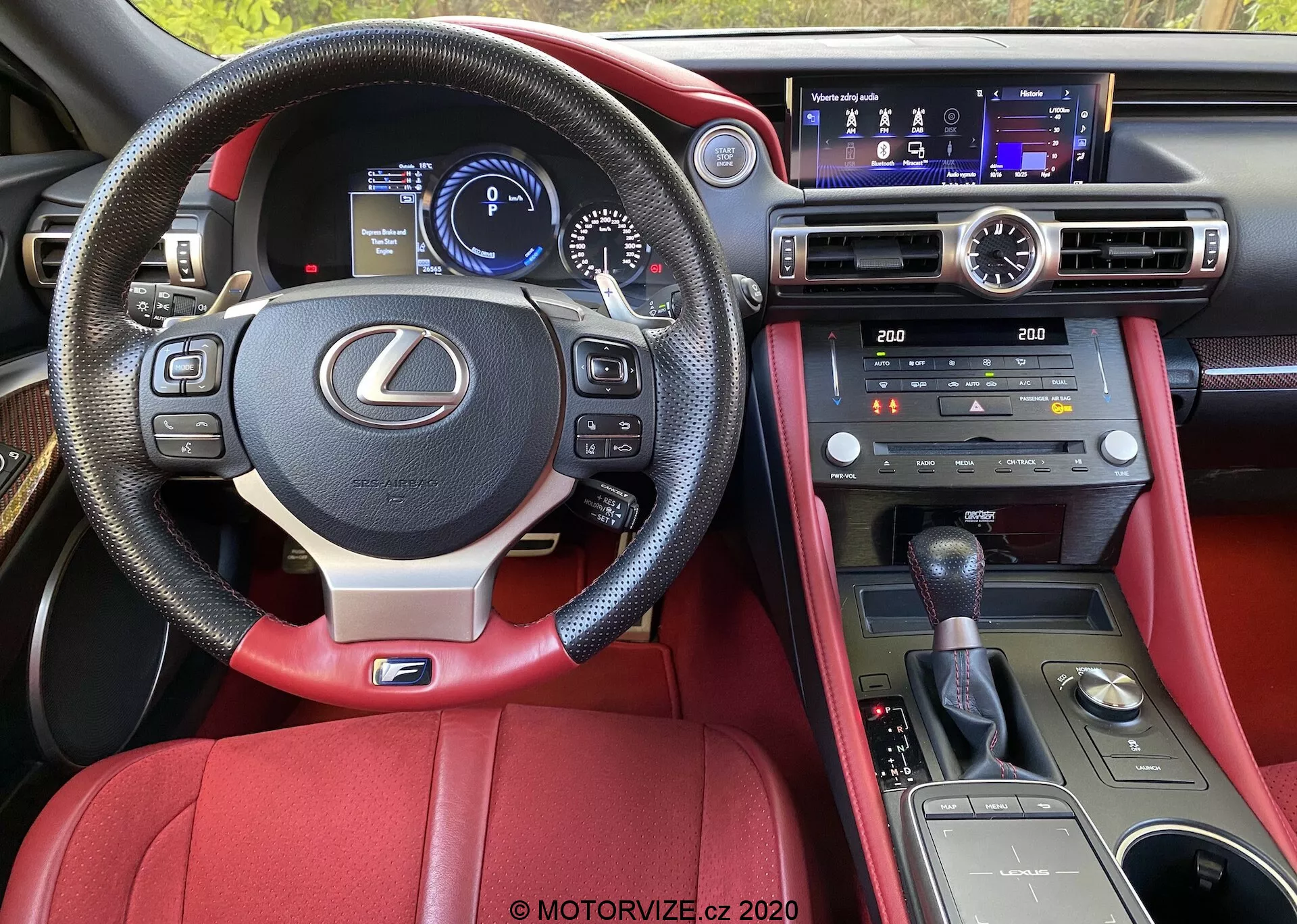 Interiörsbild av en Lexus RC 2016 från förarens perspektiv, som framhäver den läderklädda ratten med monterade kontroller, digitala instrumentbrädan, mittkonsol med multifunktionsdisplay och klimatkontroller, manuell växelspak, röd läderklädsel och avancerade teknikfunktioner.