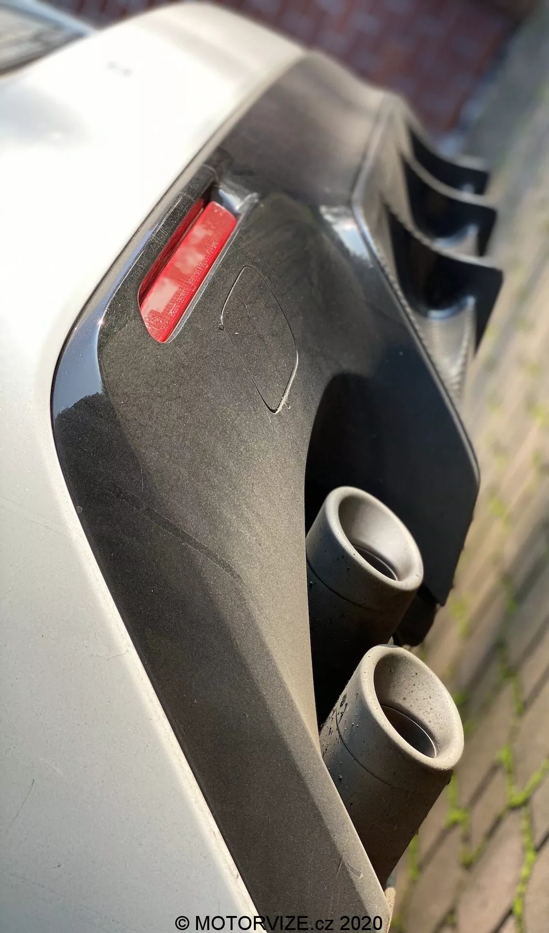 Närbild, vinklad bakifrån av en 2016 Lexus RC-sportbil med fokus på de dubbla metalliska avgasrören och bakre aerodynamiska diffusorn, med vit kaross-panel och rött bakljus synligt. Avgassystemet och diffusorn framhäver prestanda- och aerodynamiska egenskaper, fångat från ett lågt perspektiv med ett litet skärpedjup.